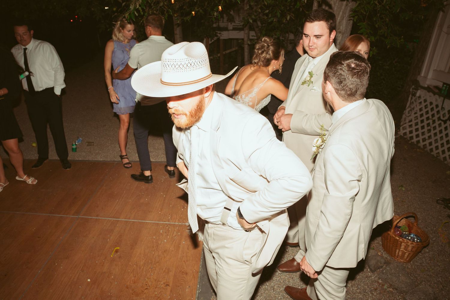Wedding guests in formal wear and cowboy hats dancing at outdoor reception.