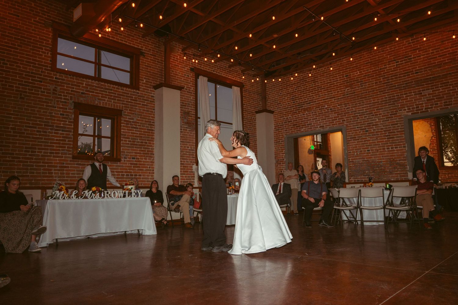 A romantic dance in a rustic brick venue with twinkling lights and white-dressed tables.