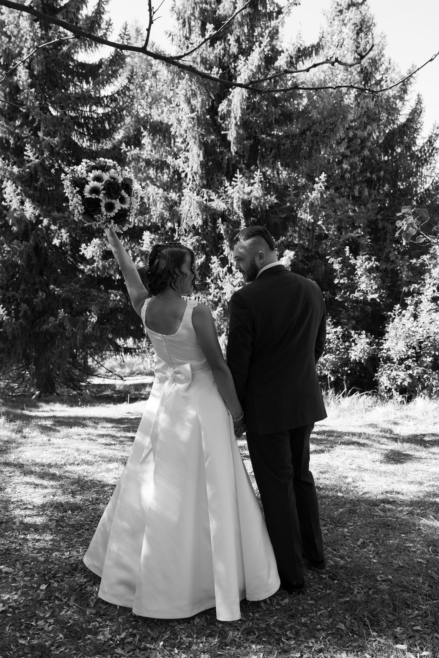 Wedding couple poses in formal attire among evergreen trees for artistic photo sequence.