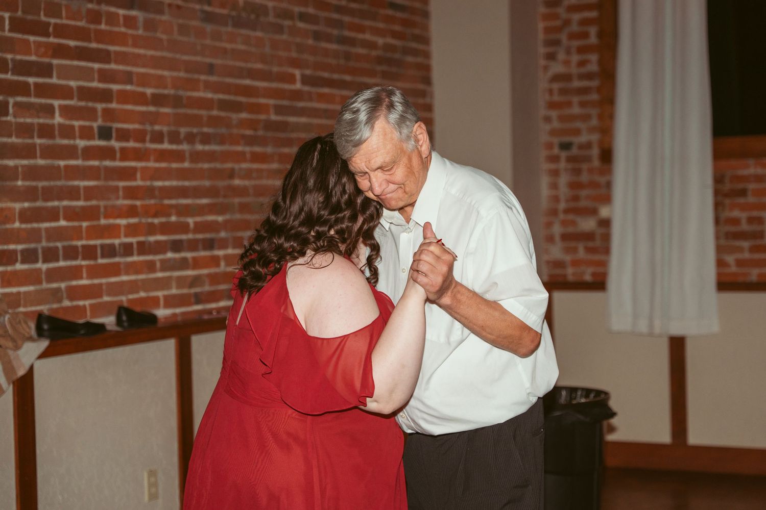 A couple dances together at a wedding reception in a brick-walled venue.