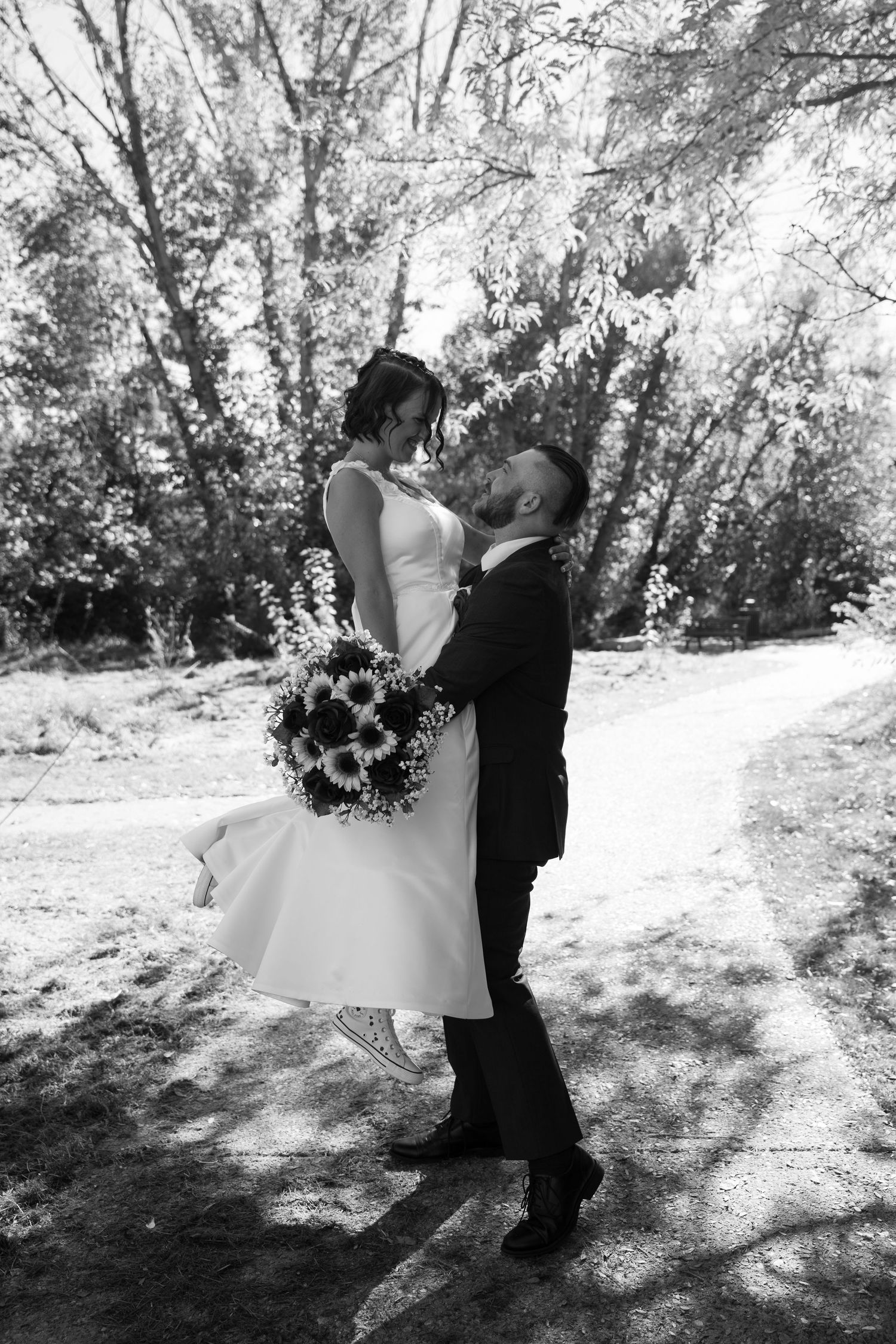 A black and white wedding photo capturing an intimate moment between newlyweds on a wooded path.