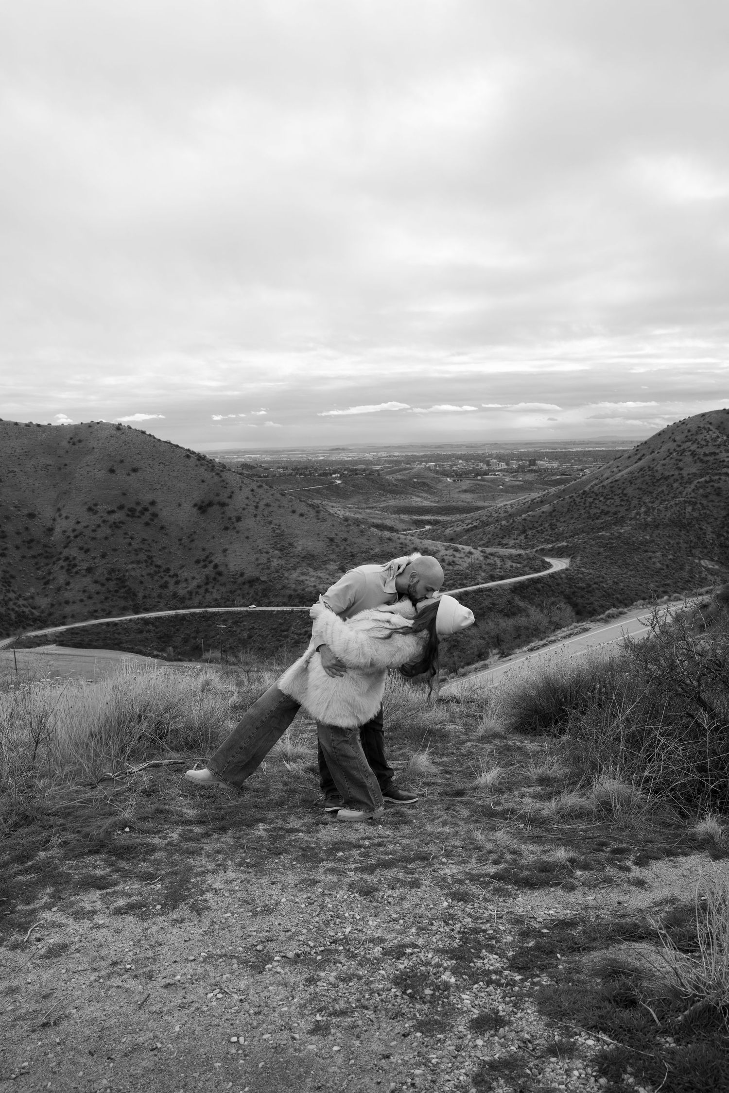 Black and white landscape photo of a couple posing dramatically on a hilltop.