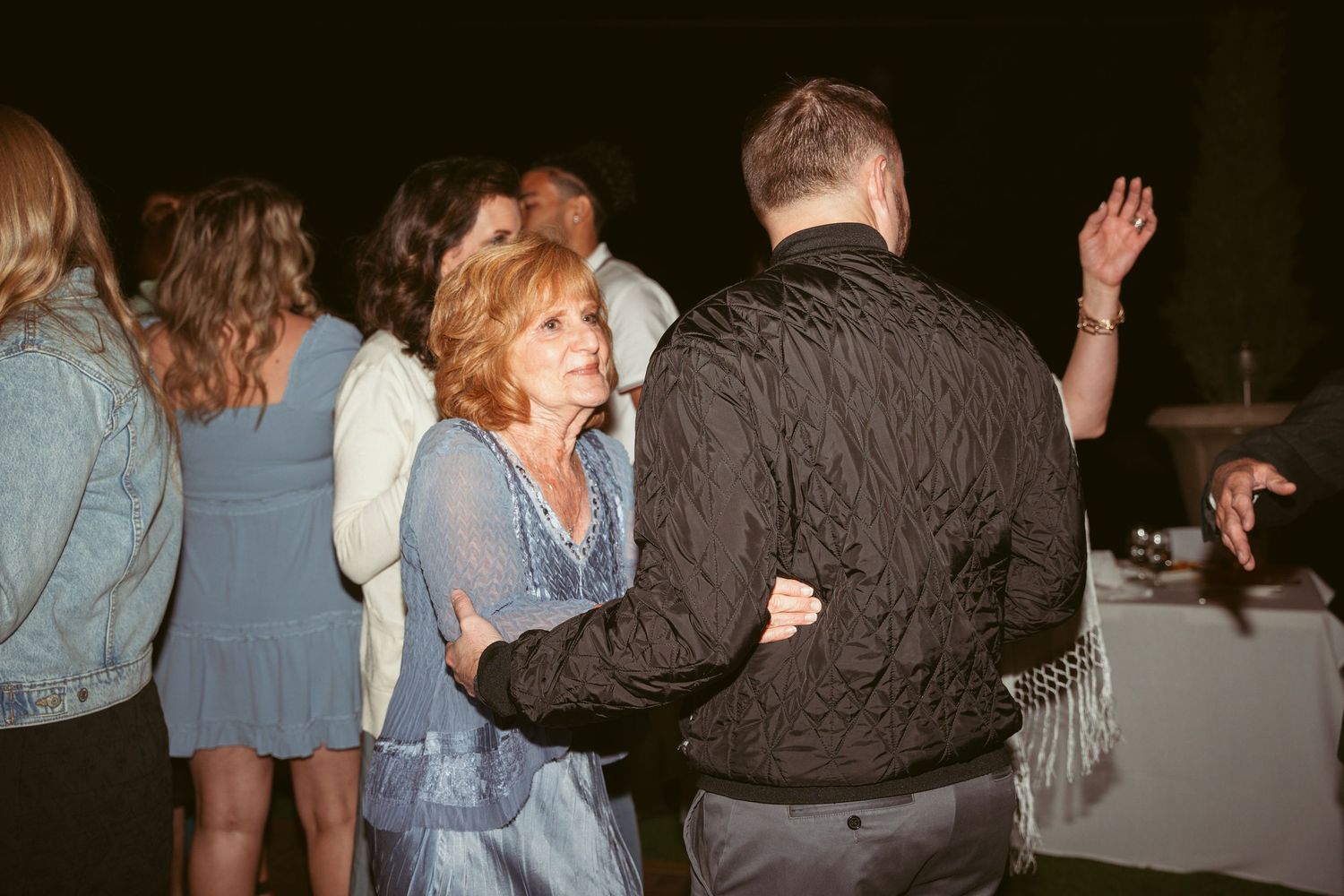 Couples dancing together at a dimly lit party under string lights with casual and formal attire.
