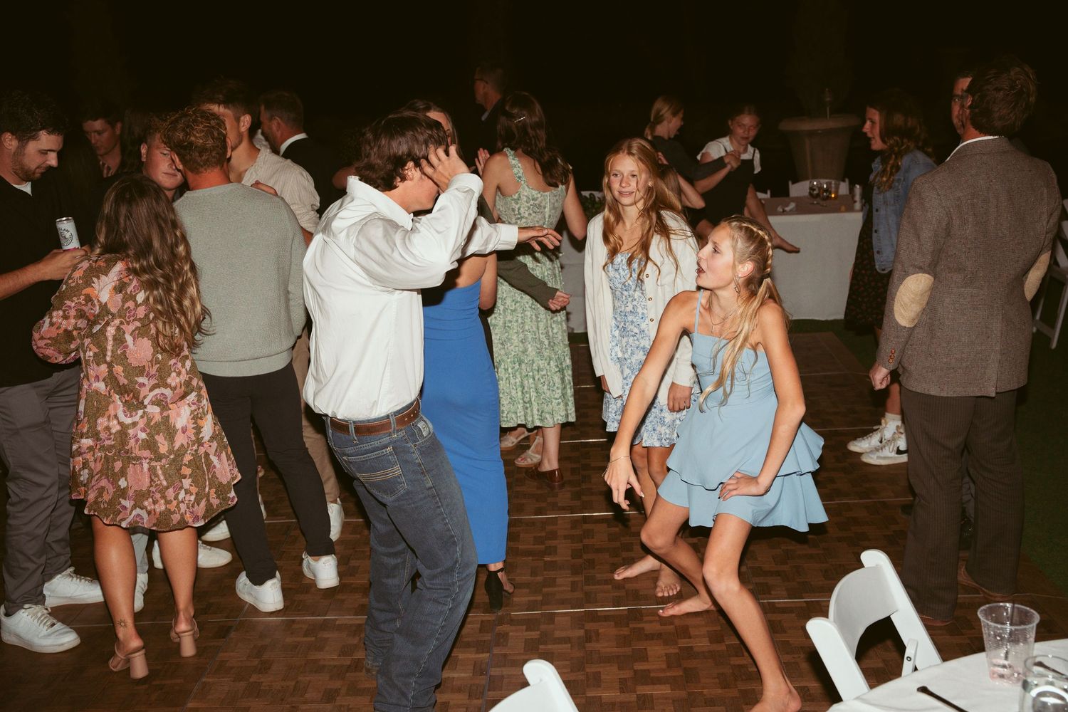 Guests dancing and celebrating on a wooden dance floor under ambient lighting at an evening event.