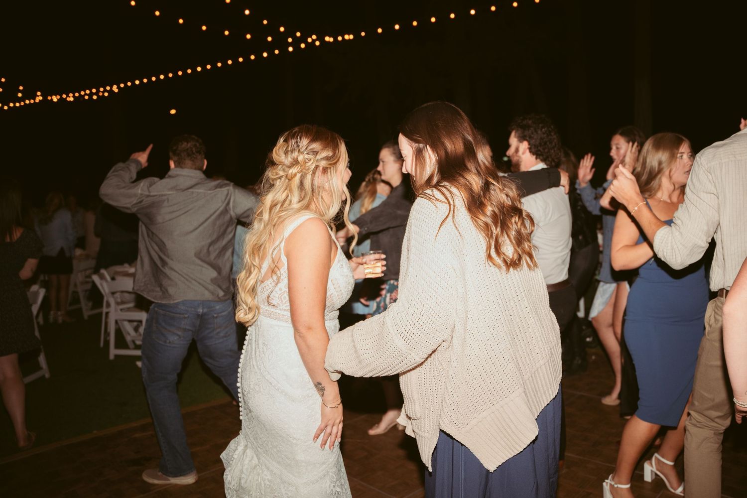 Party guests dancing and celebrating under string lights at an outdoor evening event.