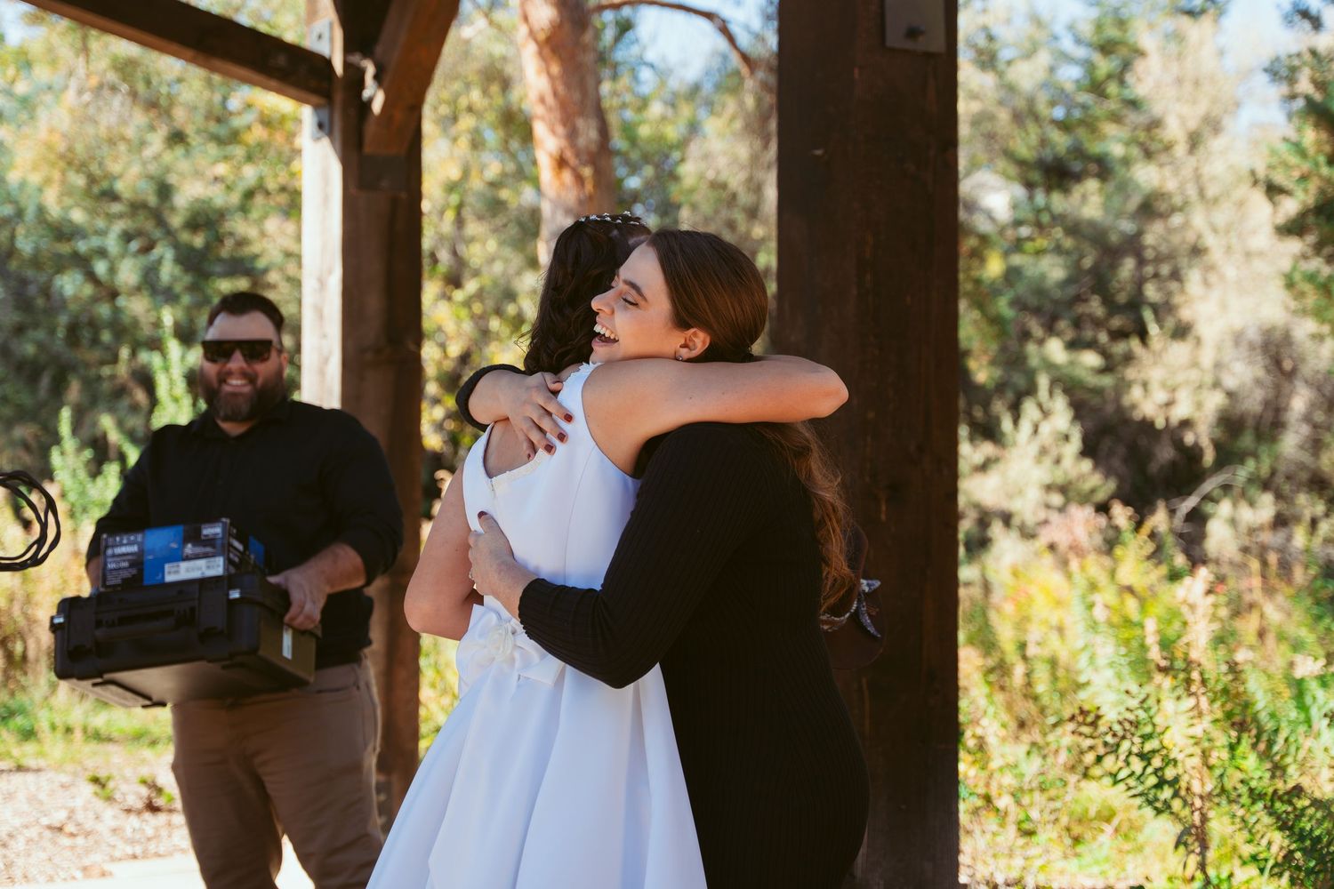 Emotional embraces shared during outdoor wedding ceremony under wooden pergola.