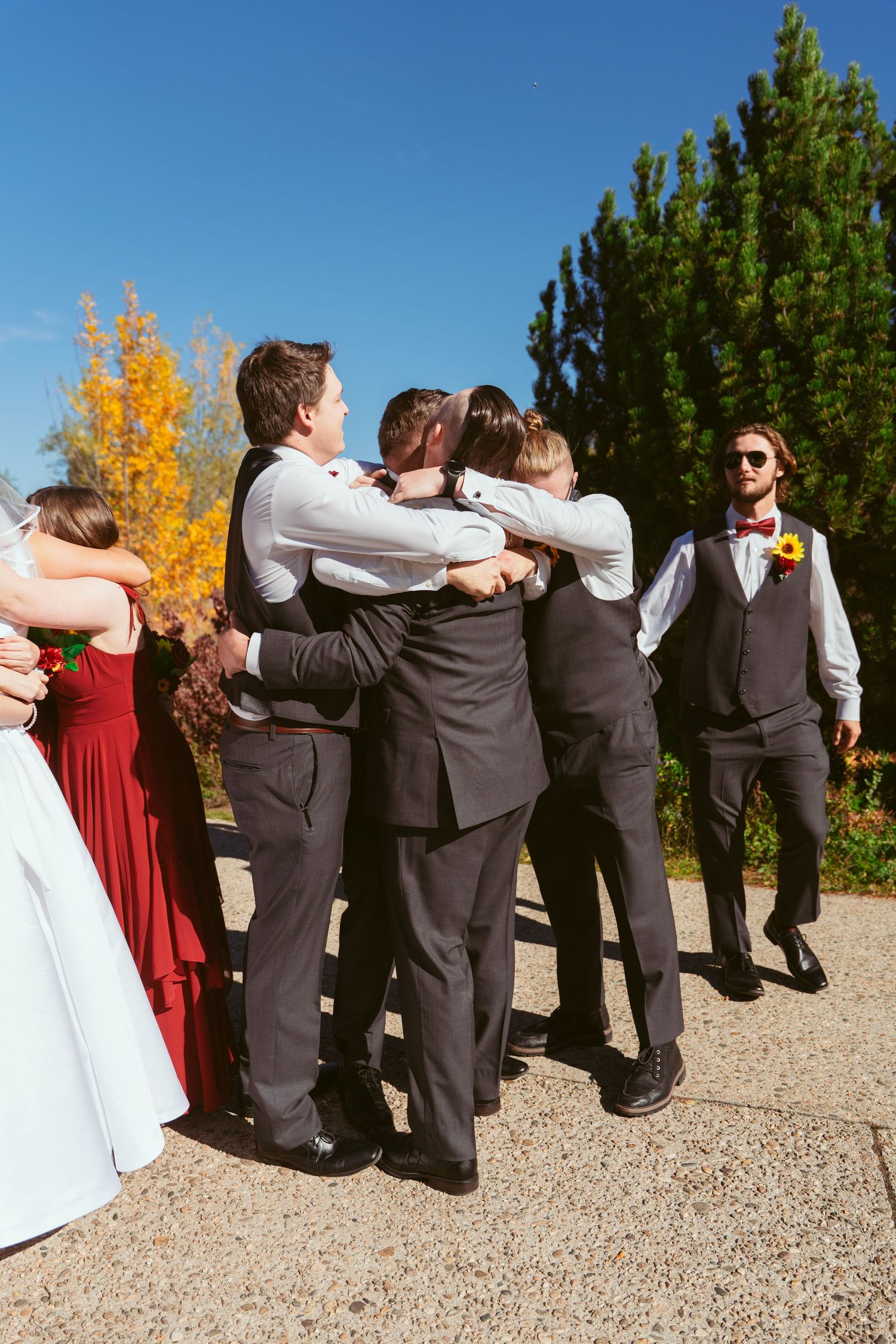 Wedding party lines up for creative photo on gravel path with autumn foliage in background.