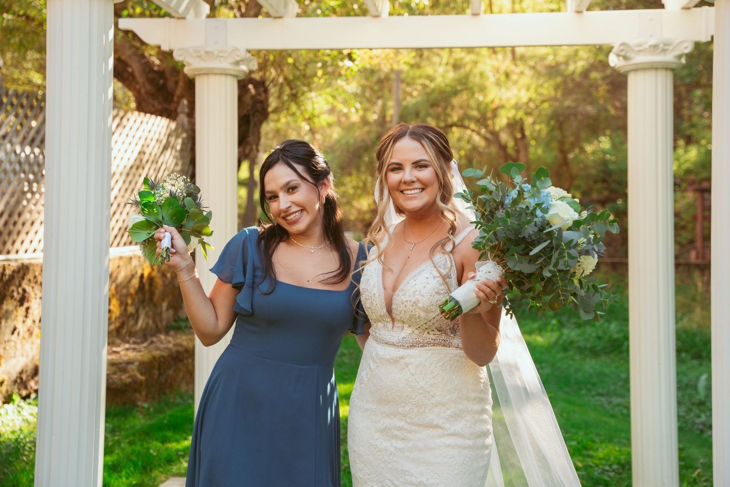 Wedding party members in navy blue and white posing under garden pergola.