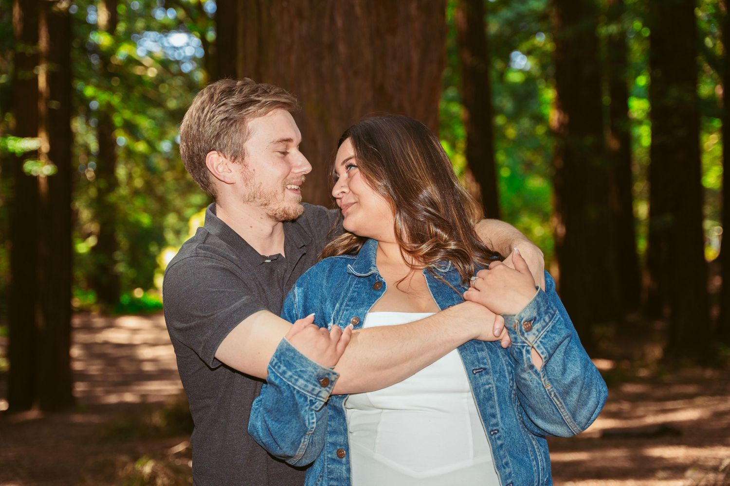 A romantic embrace captured in a serene forest with dappled sunlight filtering through the trees.