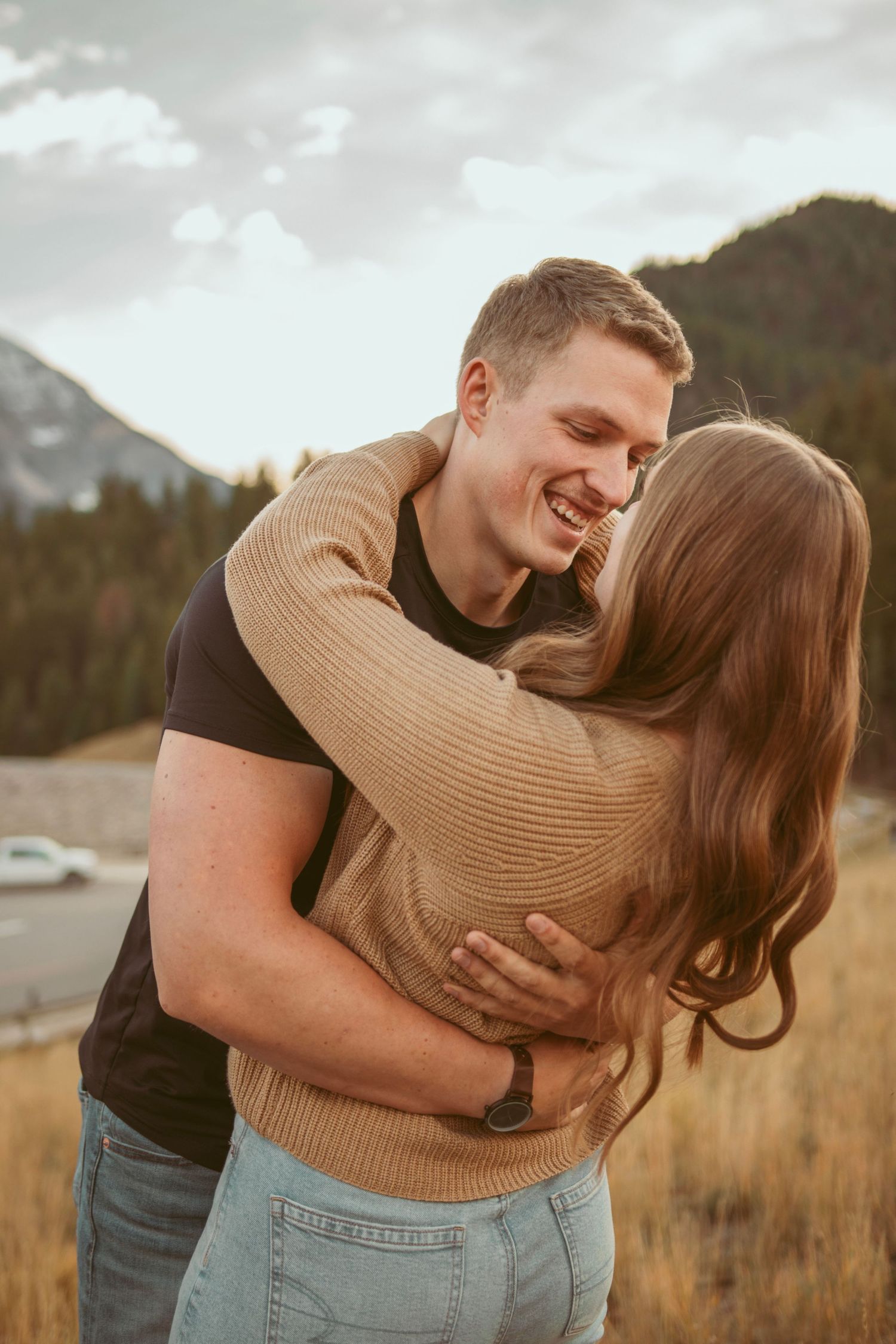 Playful couple embracing in mountain field during sunset.