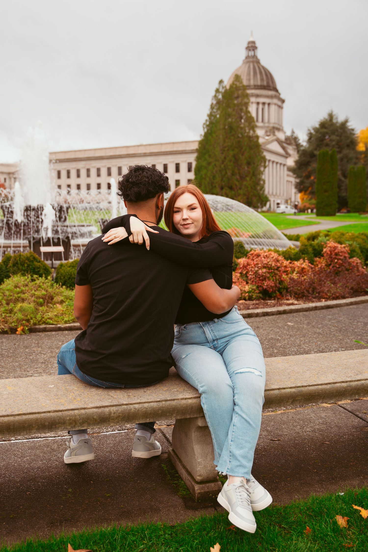 Couple sitting together on stone ledge with government building in background.