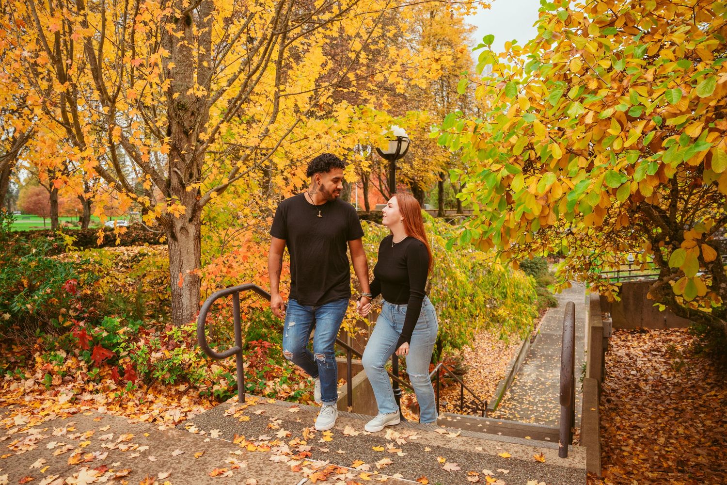 Couple walking together on a path surrounded by vibrant autumn trees with golden yellow leaves.
