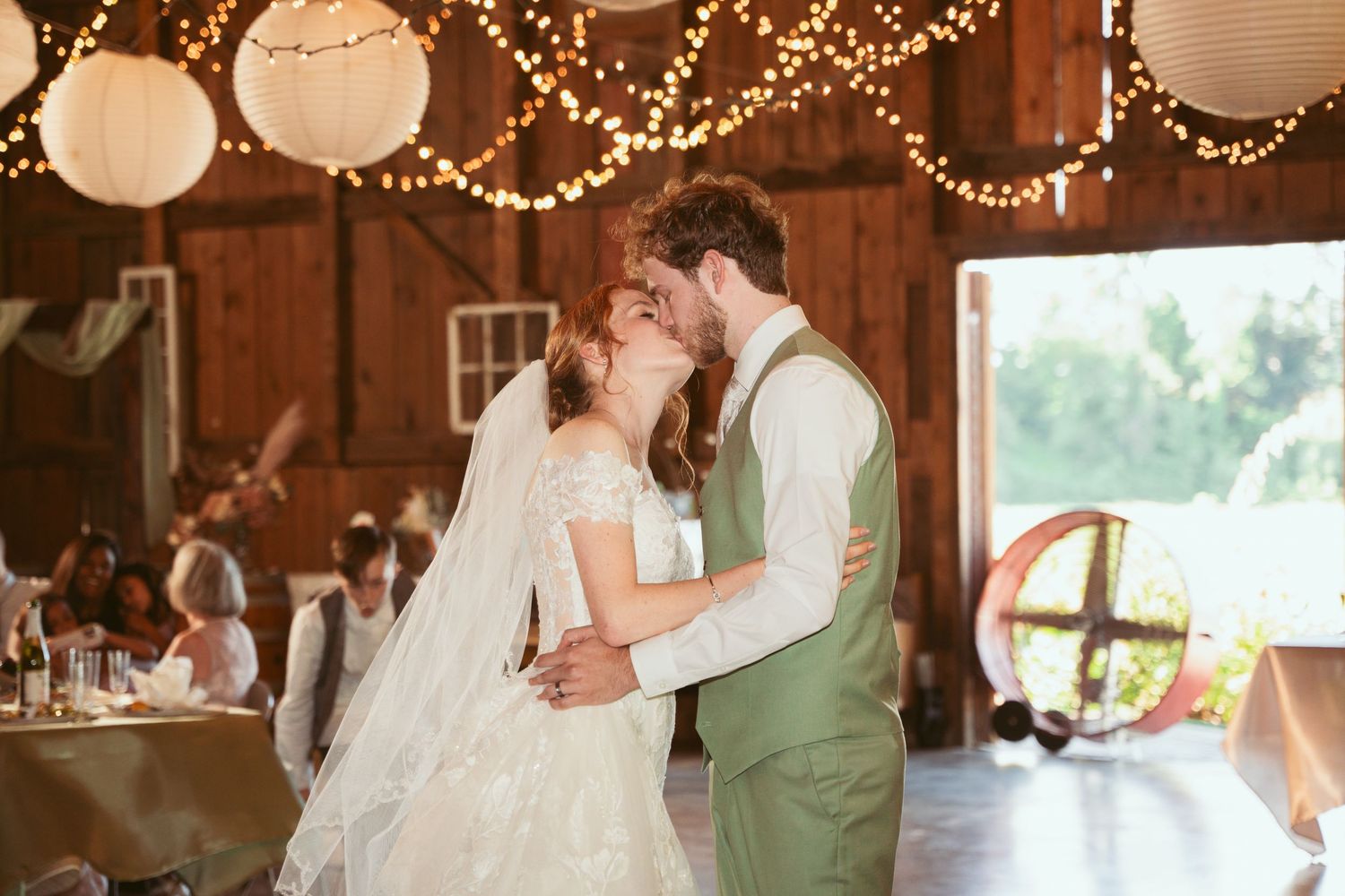 Romantic first dance in a wooden barn decorated with warm fairy lights and white paper lanterns.