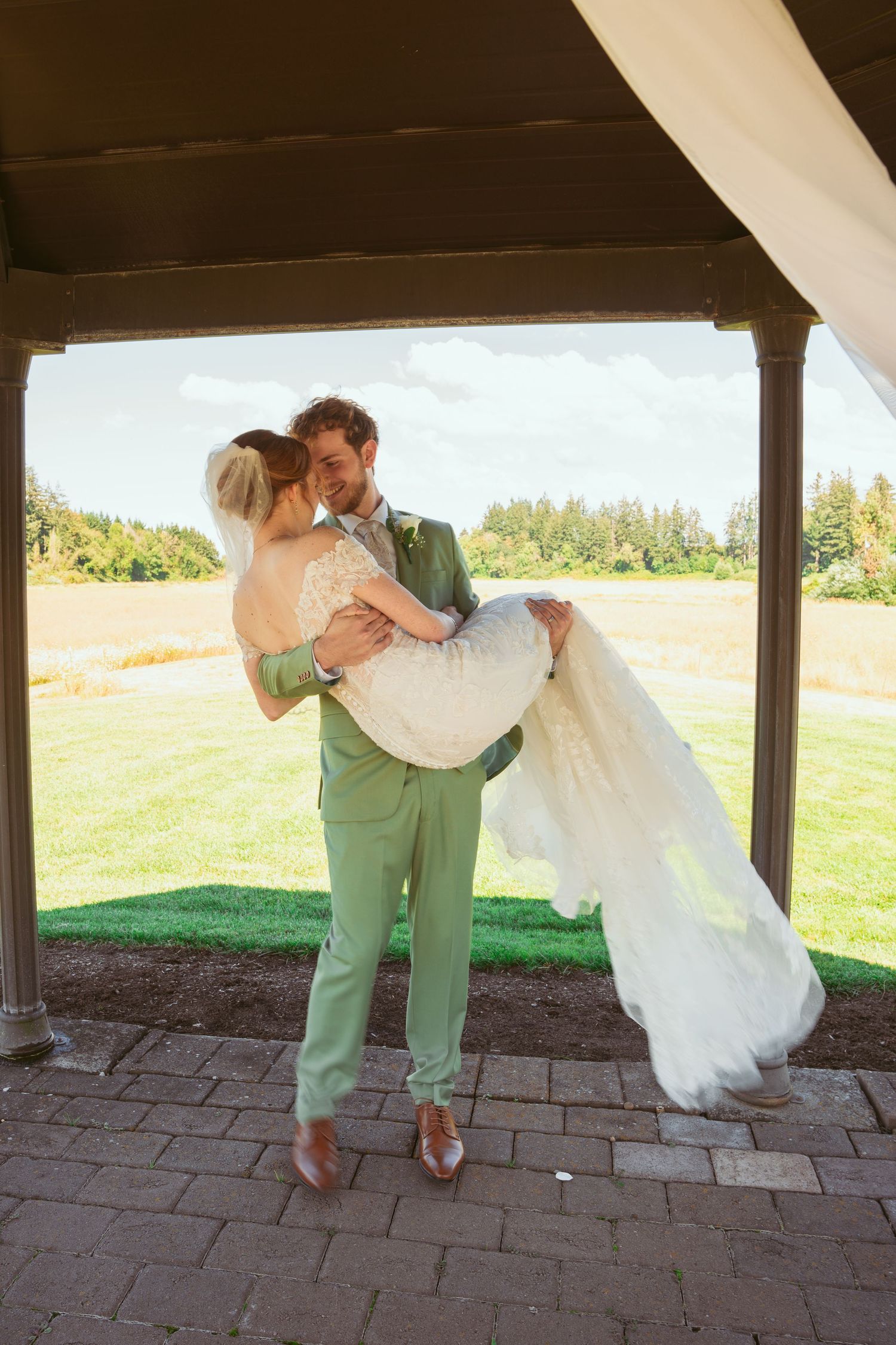 A romantic dip sequence under a covered porch with bride in white dress and groom in sage green suit.