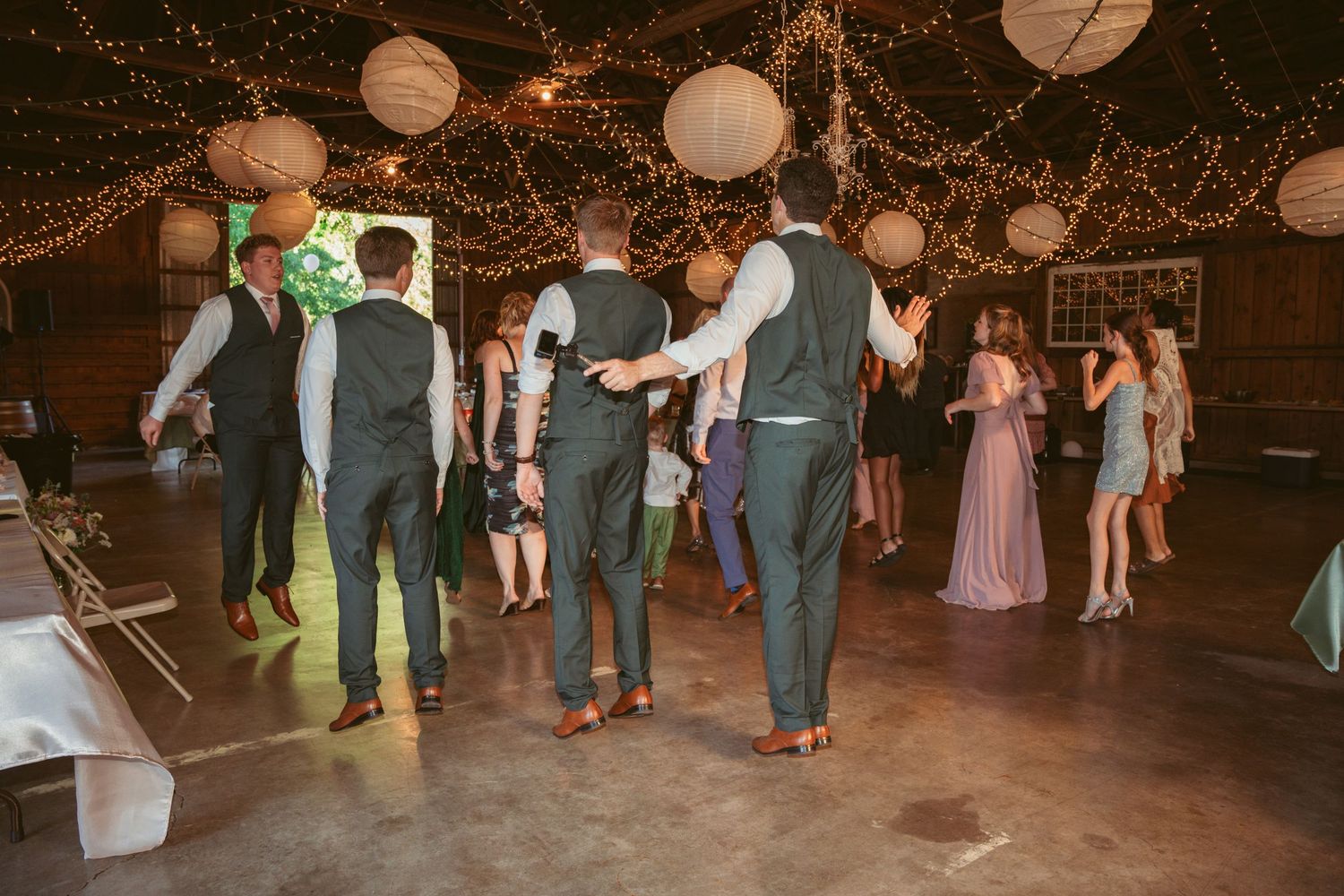 Wedding guests line dancing on a wooden floor under warm string lights and lanterns.