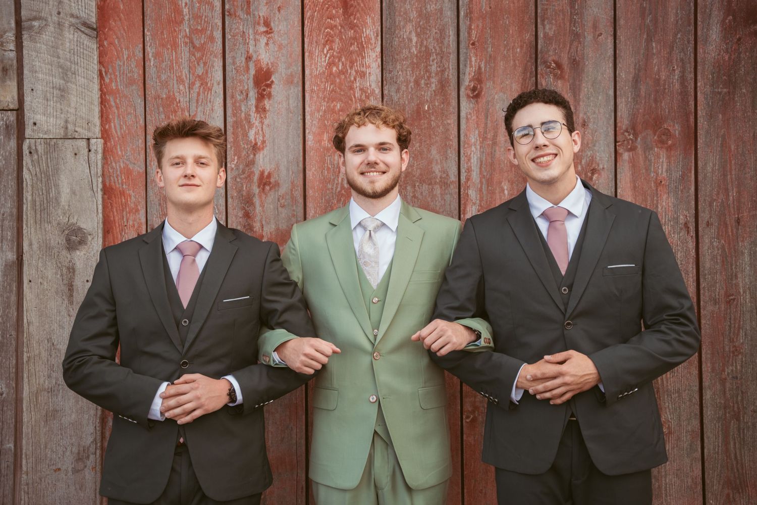 Wedding party lined up in formal attire against rustic barn wall for professional photos.
