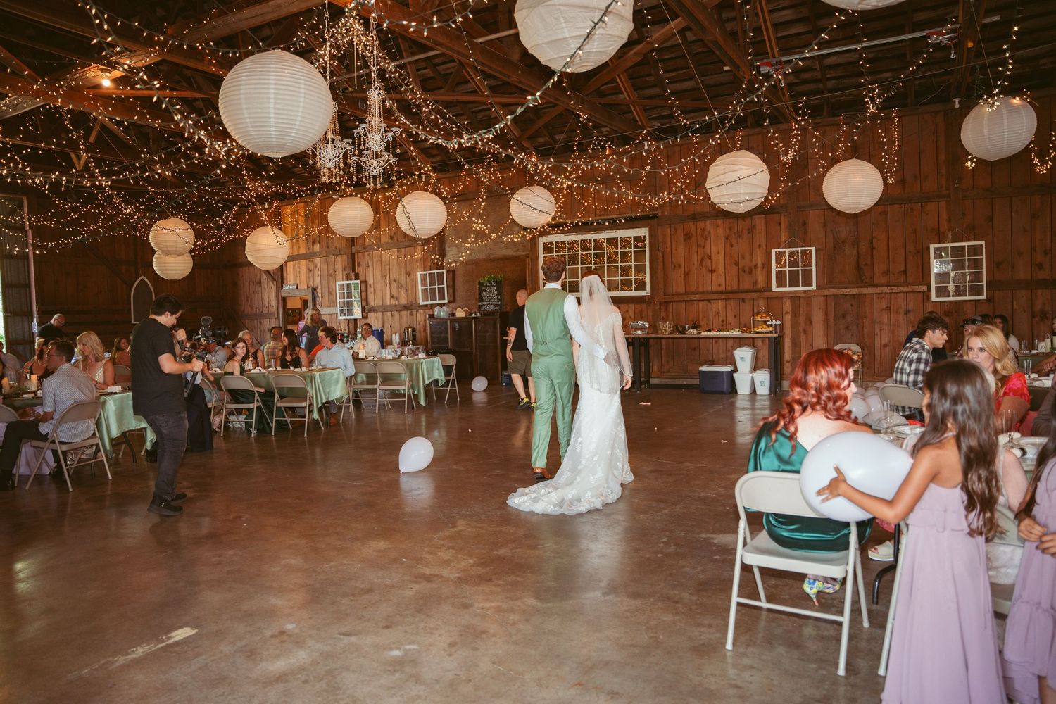 Wedding celebration in progress inside a barn with string lights and paper lantern decorations.