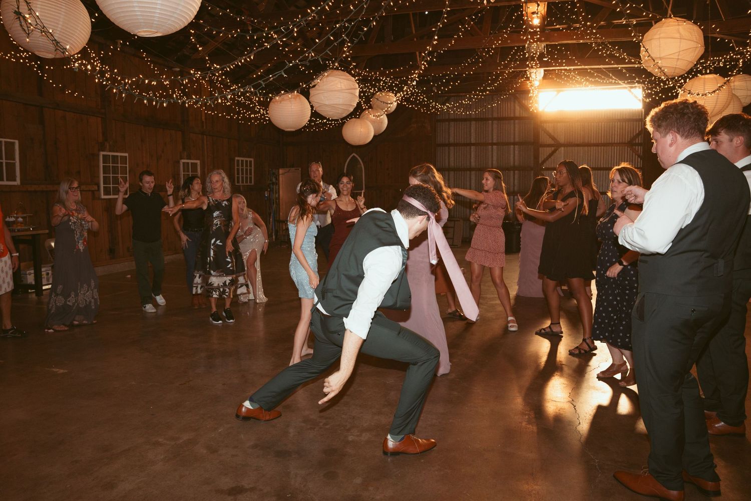 Couples dancing together under romantic string light canopy at rustic indoor venue.