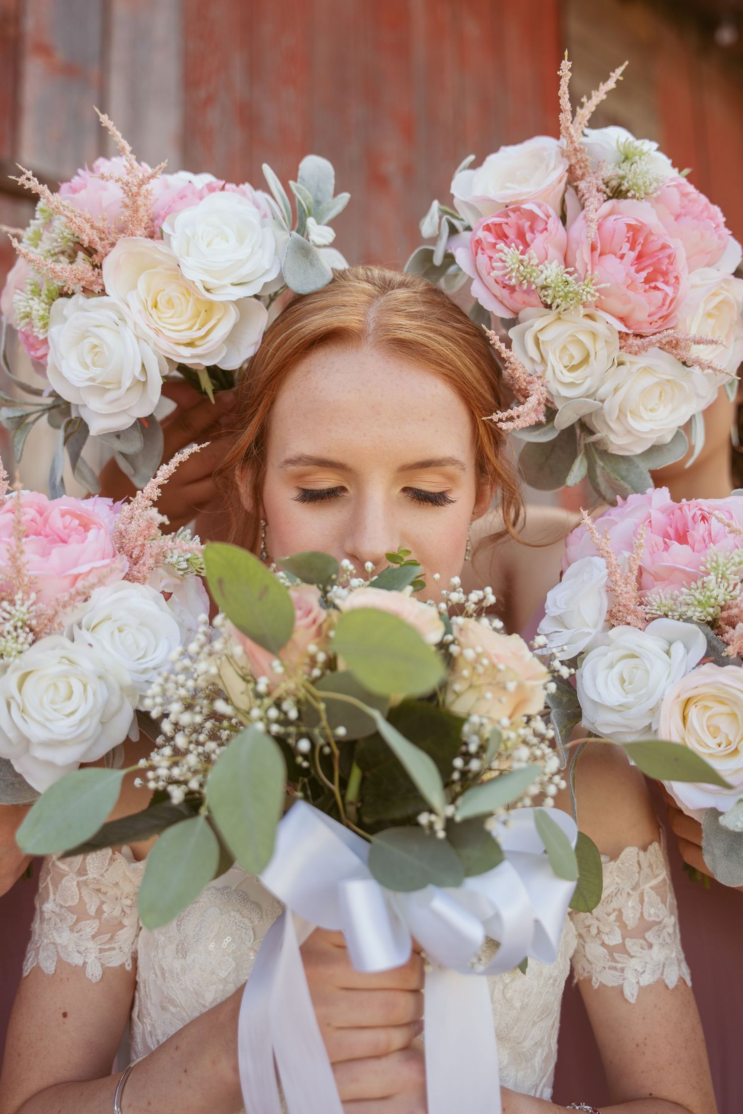 Beautiful wedding bouquets featuring pink and white roses with eucalyptus leaves against a rustic red barn backdrop.