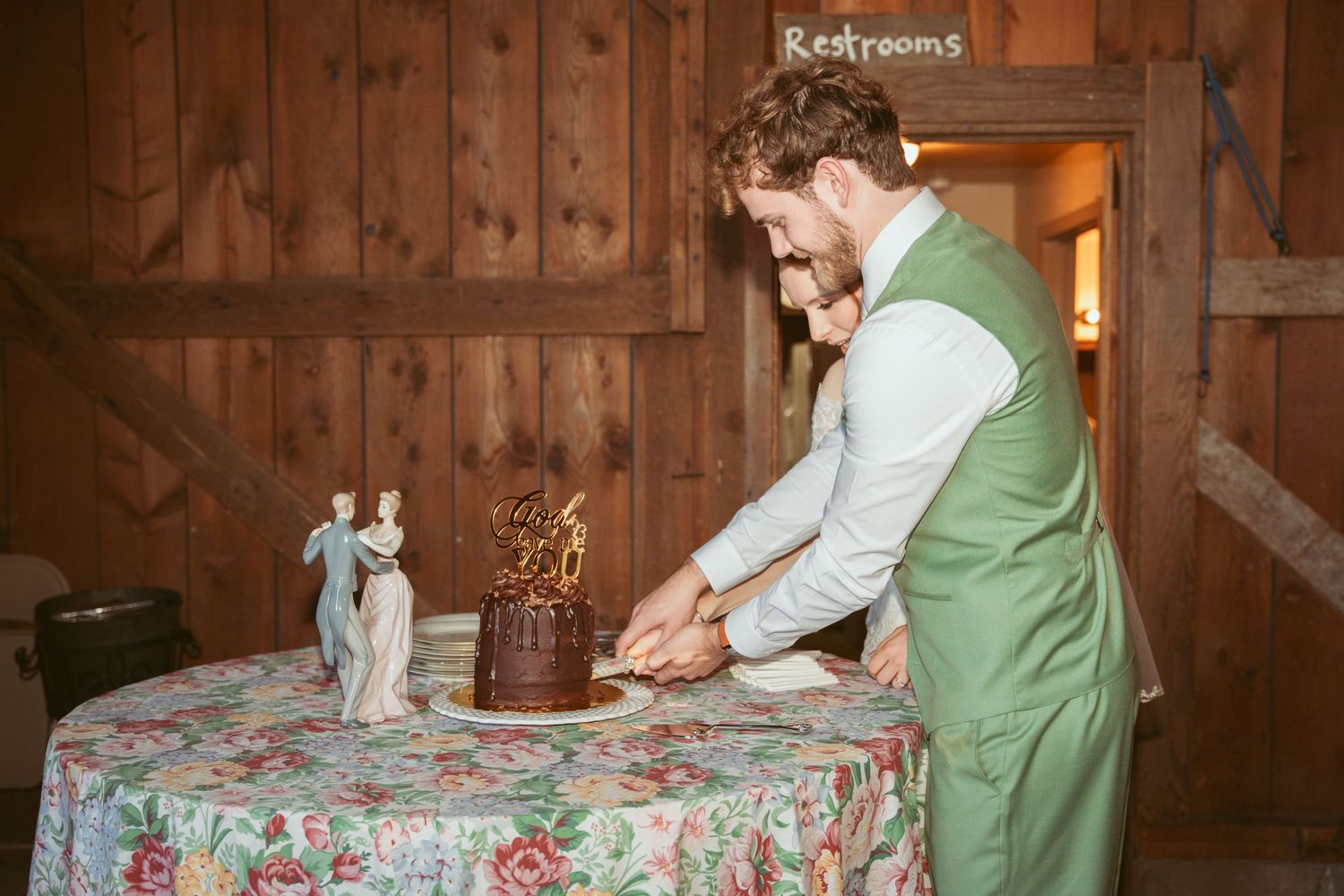 Wedding cake cutting moment captured in rustic barn setting with wooden walls.