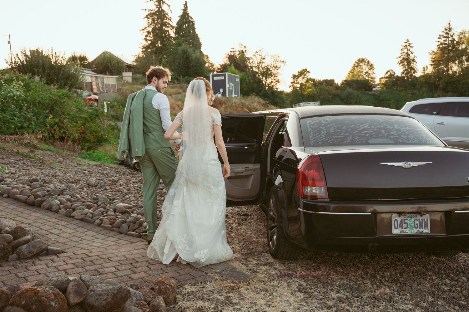 Wedding couple and guests walking along a gravel path outside the venue at sunset.