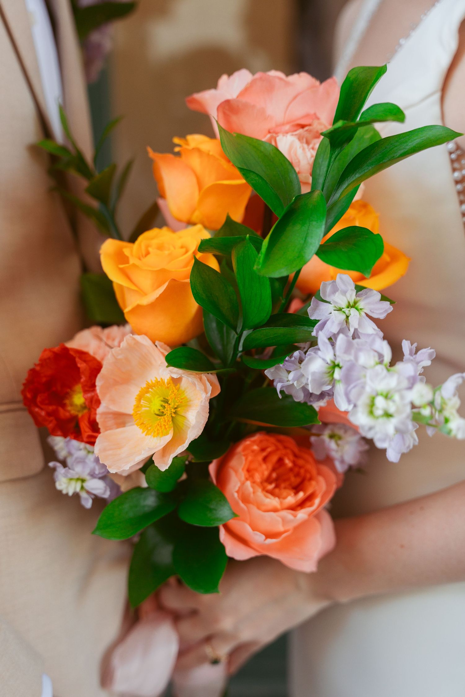 Vibrant coral and peach roses with purple flowers arranged in an elegant wedding bouquet.