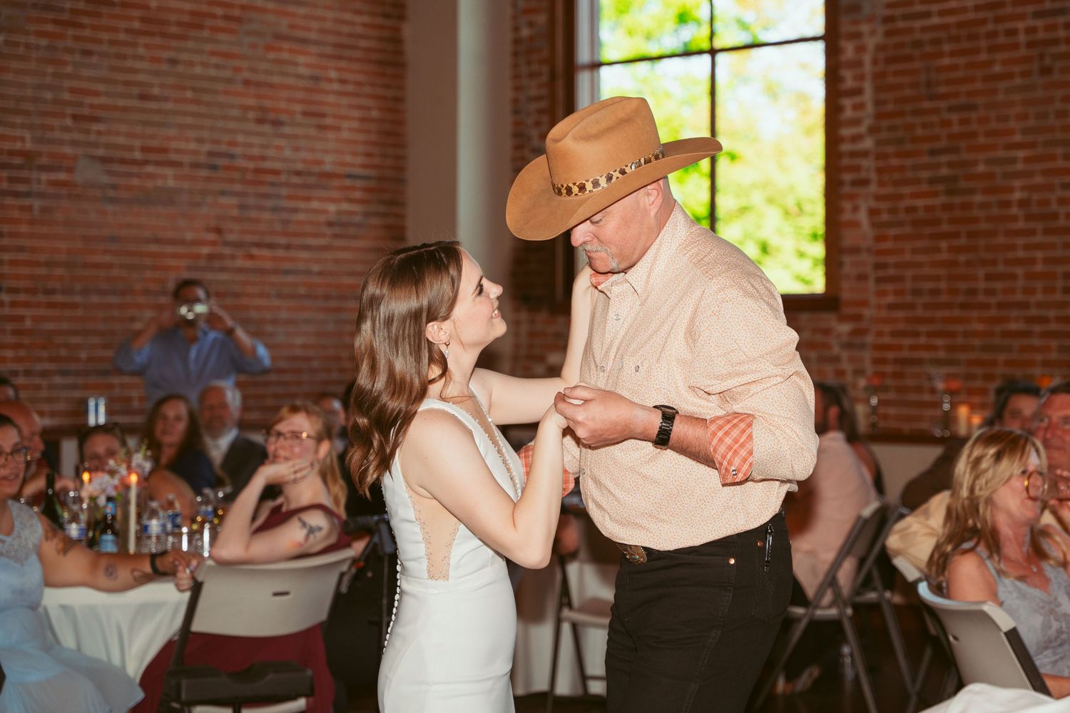 Wedding dancers execute a graceful twirl under string lights in a brick-walled venue.