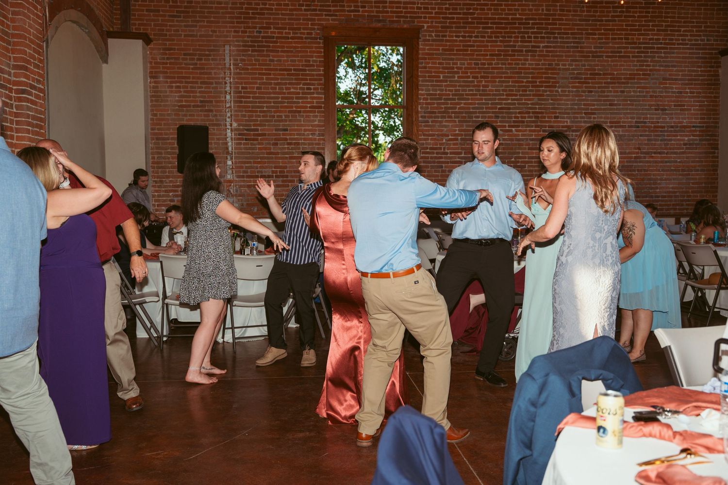 Wedding reception dance floor filled with guests dancing under twinkling lights in a brick venue.