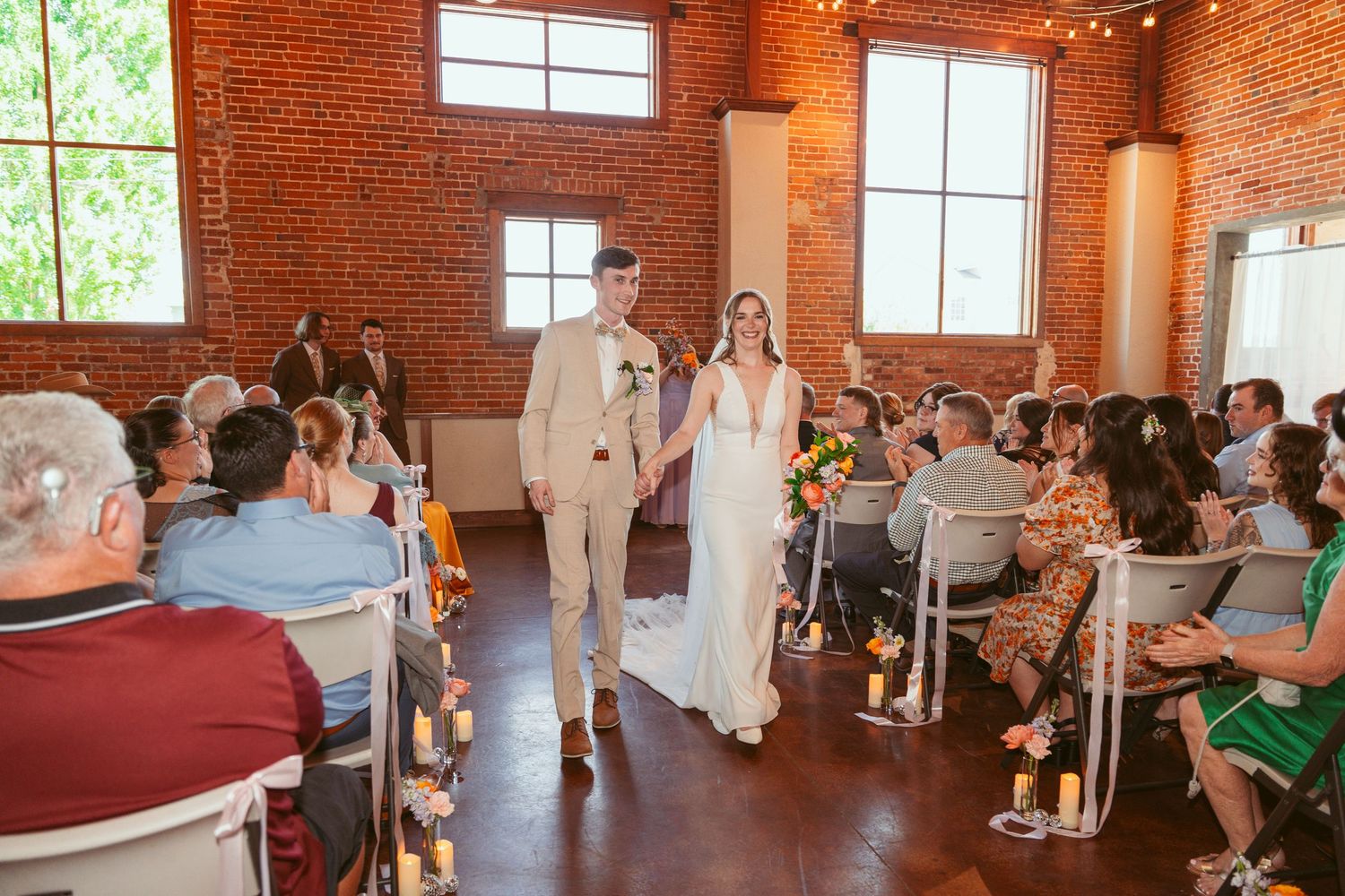 Full view of wedding ceremony space showing guests, decor, and natural light from windows.