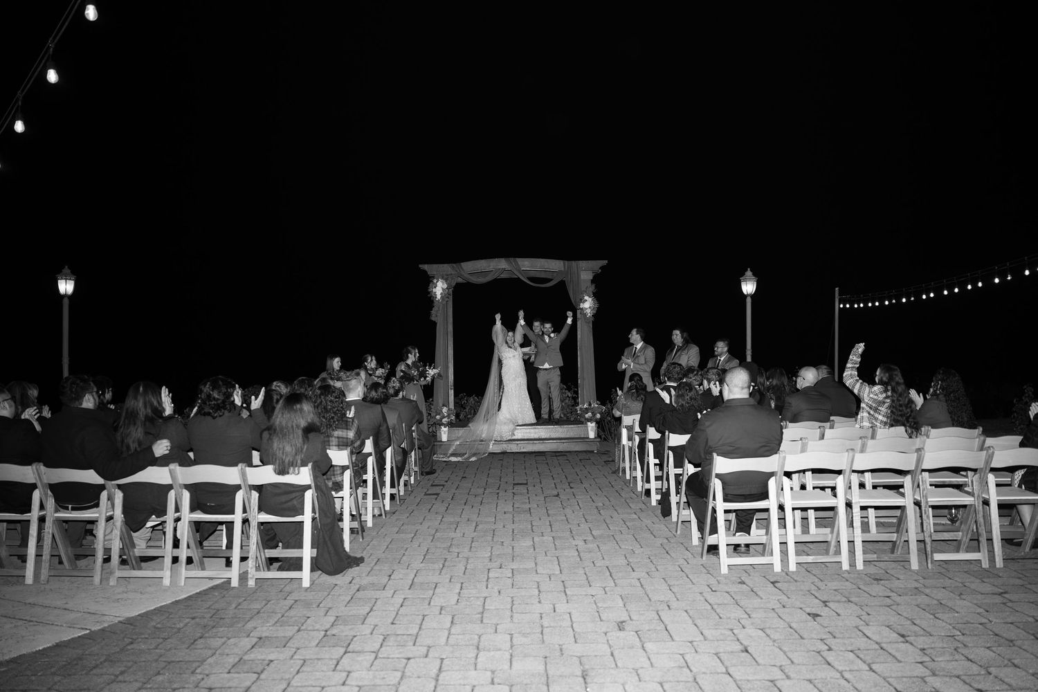 A nighttime outdoor wedding ceremony setup with chairs and an illuminated arch.
