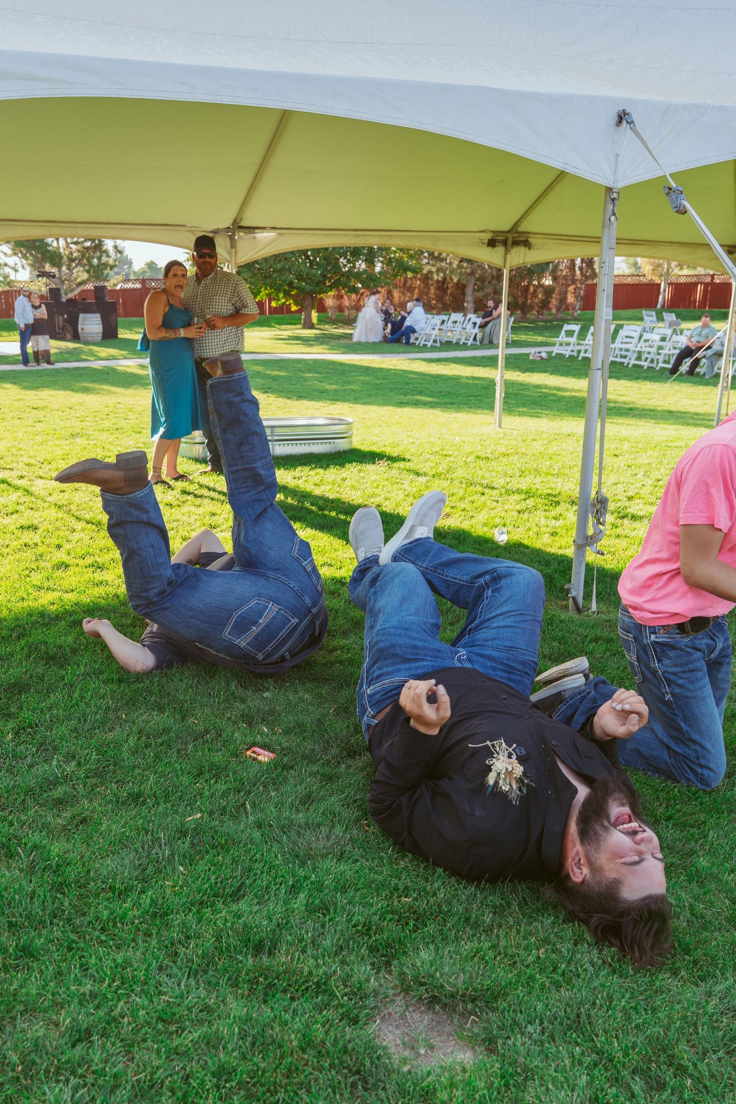 People lying on grass under a white tent during an outdoor event.