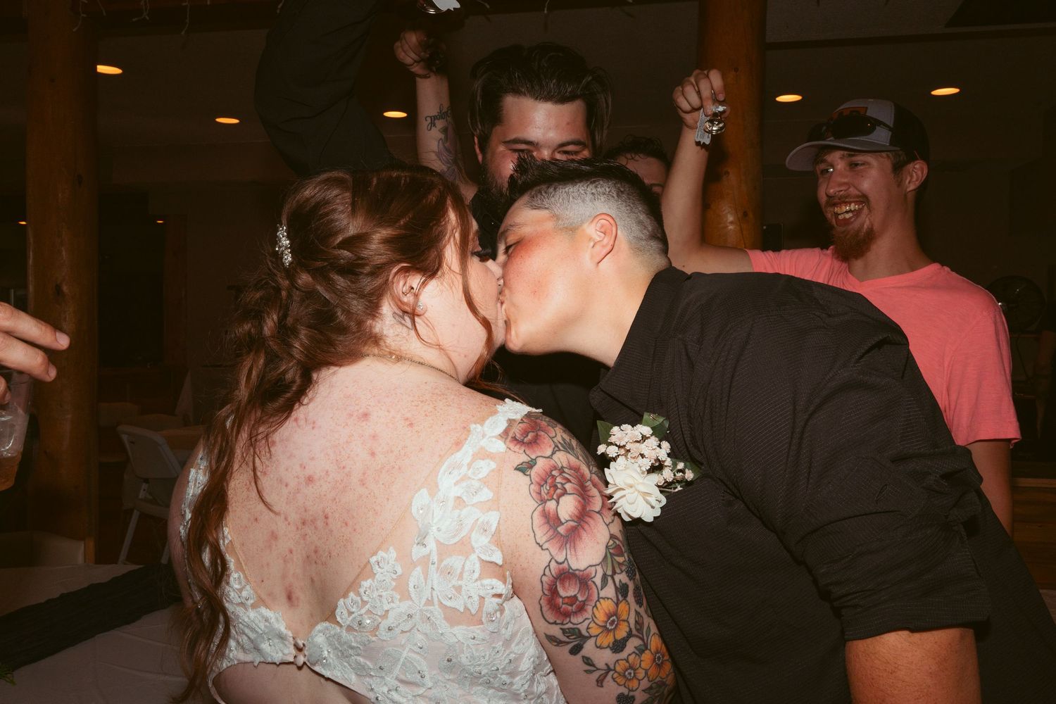 Wedding guests dance and celebrate during an indoor reception with wooden log pillars.