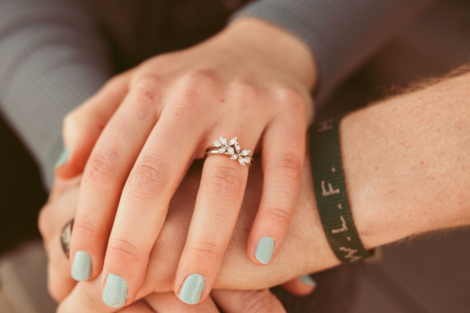 Close-up shots of hands wearing an engagement ring with light blue nail polish.