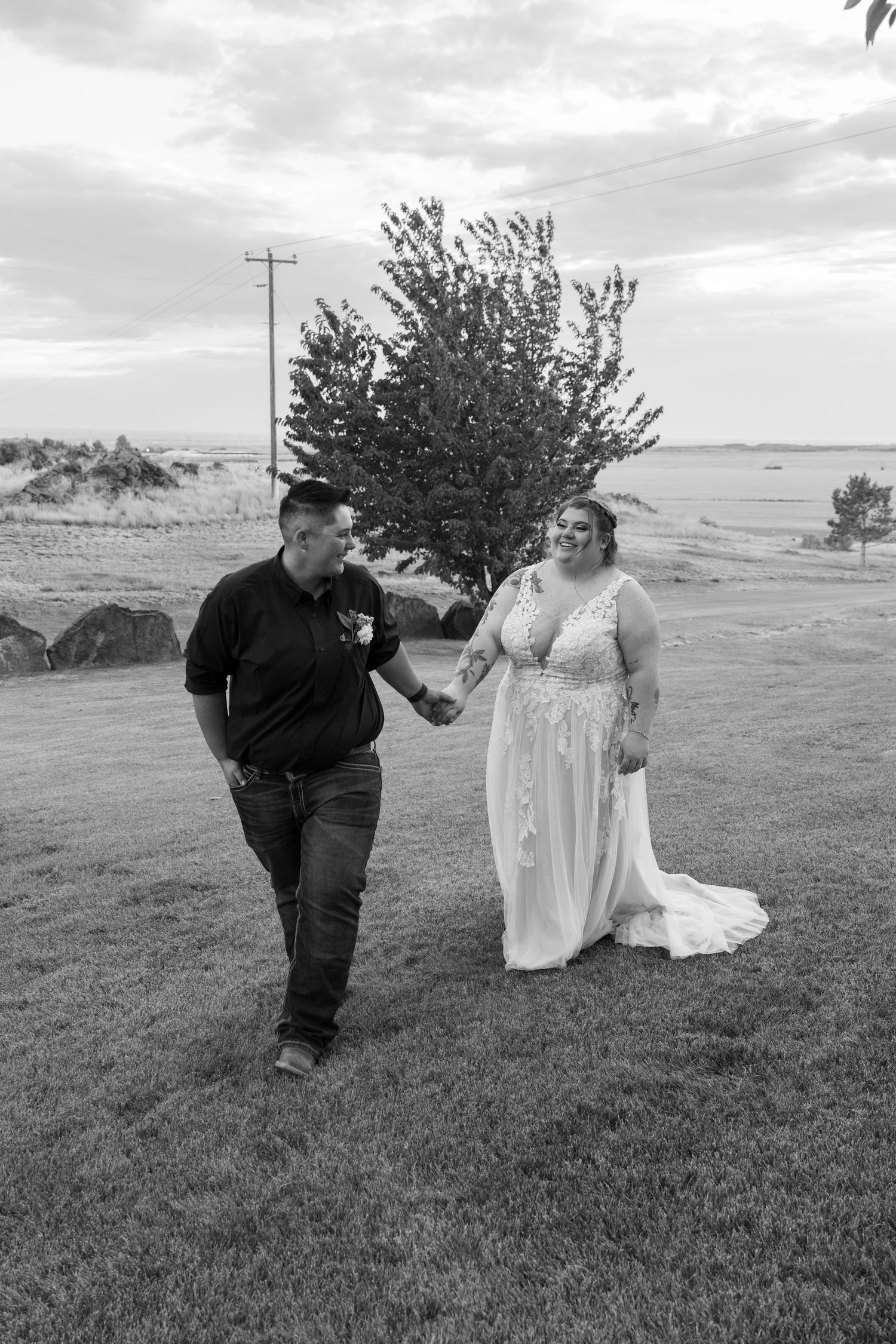 A black and white photo of newlyweds sharing a playful moment on a grassy hillside.