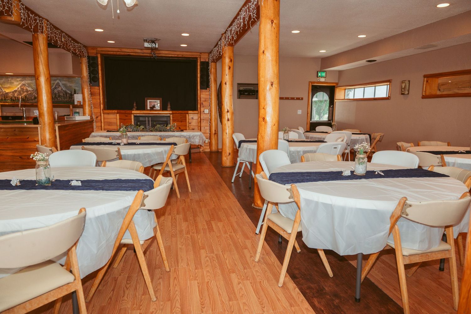 Large banquet hall with wooden floors, exposed beams, and round tables set with light blue tablecloths.