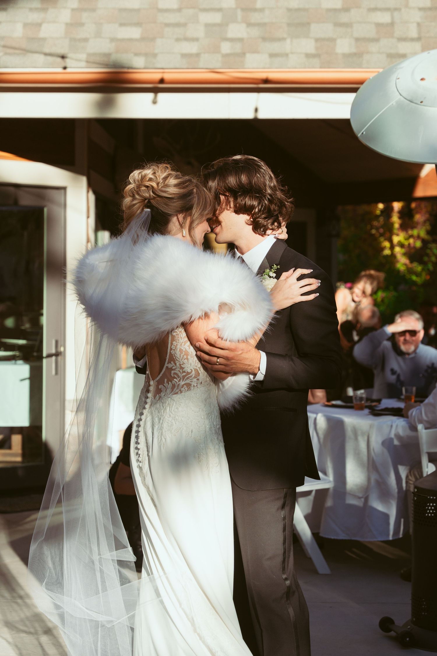 A romantic dance moment between newlyweds at their outdoor reception with guests in background.