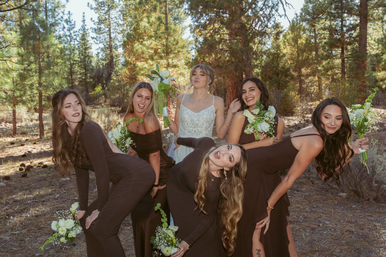 Bridal party creates dynamic poses and expressions in outdoor woodland setting.