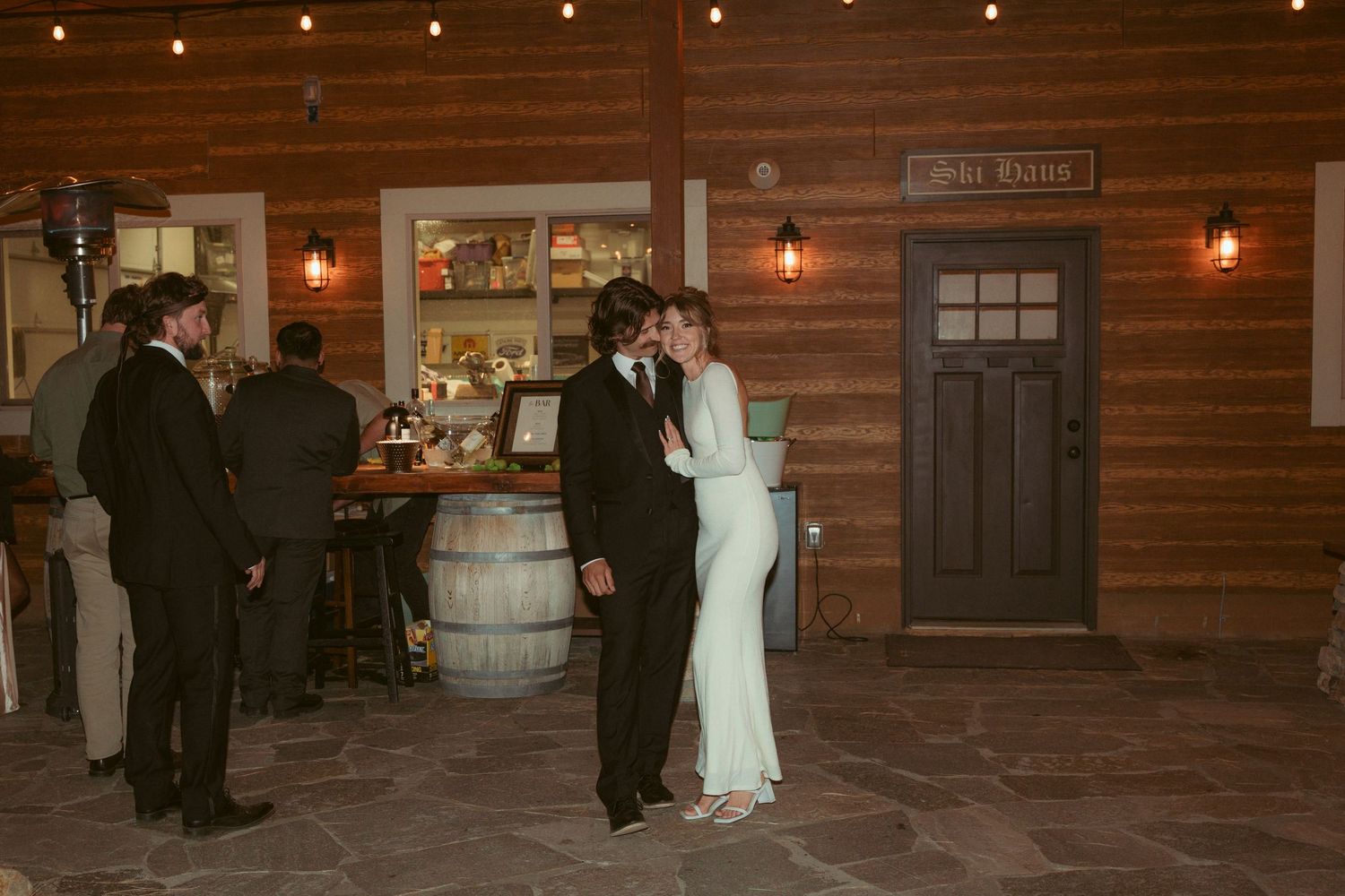 Wedding reception in a rustic wooden venue with barrel decor and string lights.