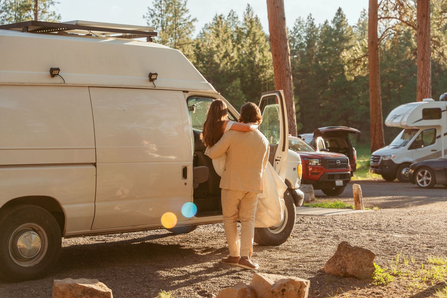 Wedding venue parking area at sunset with white vans and natural forest backdrop.