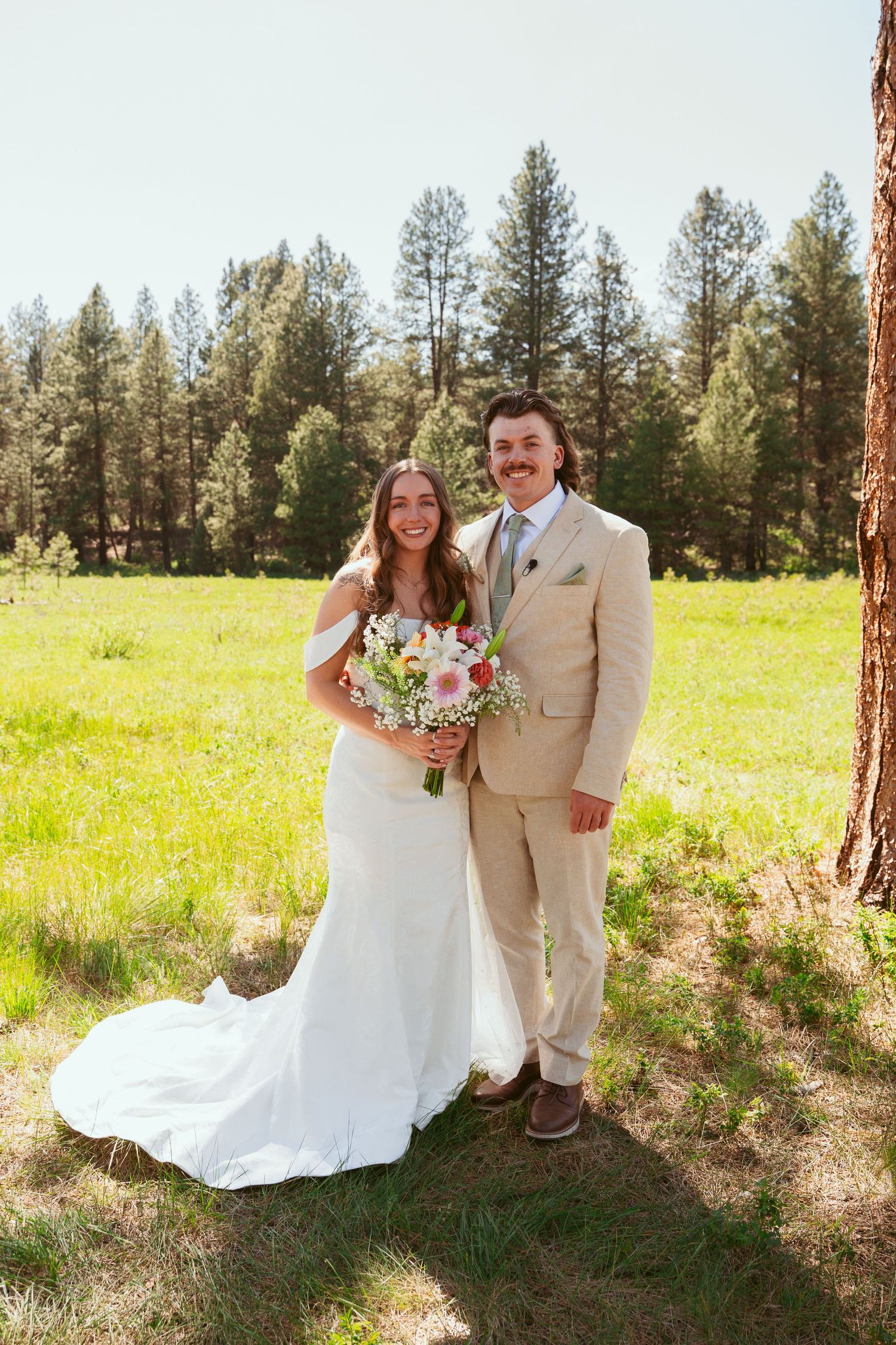Sunlit wedding portrait in front of tall pine trees.