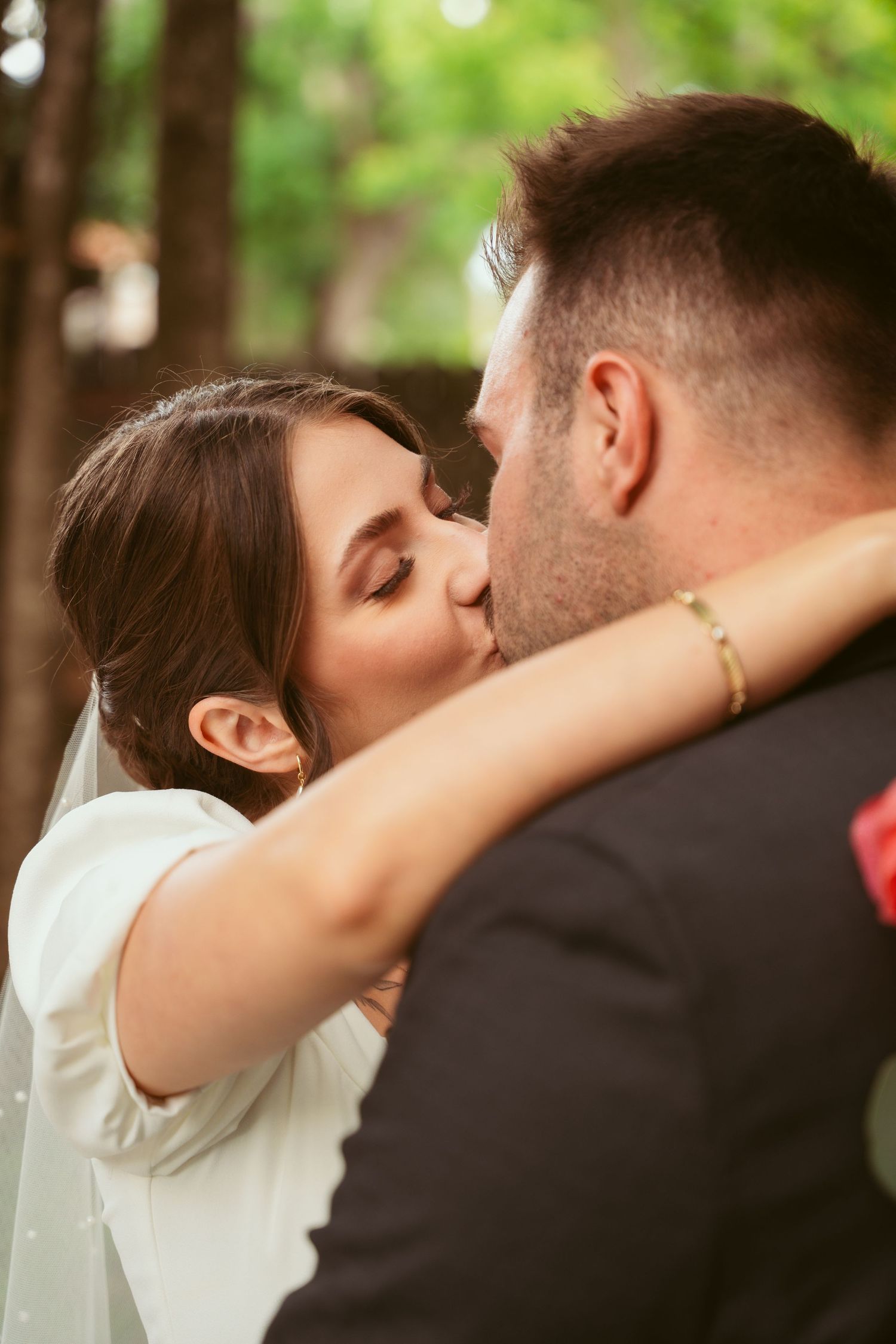 An intimate kiss shared between newlyweds in a sunlit outdoor setting.