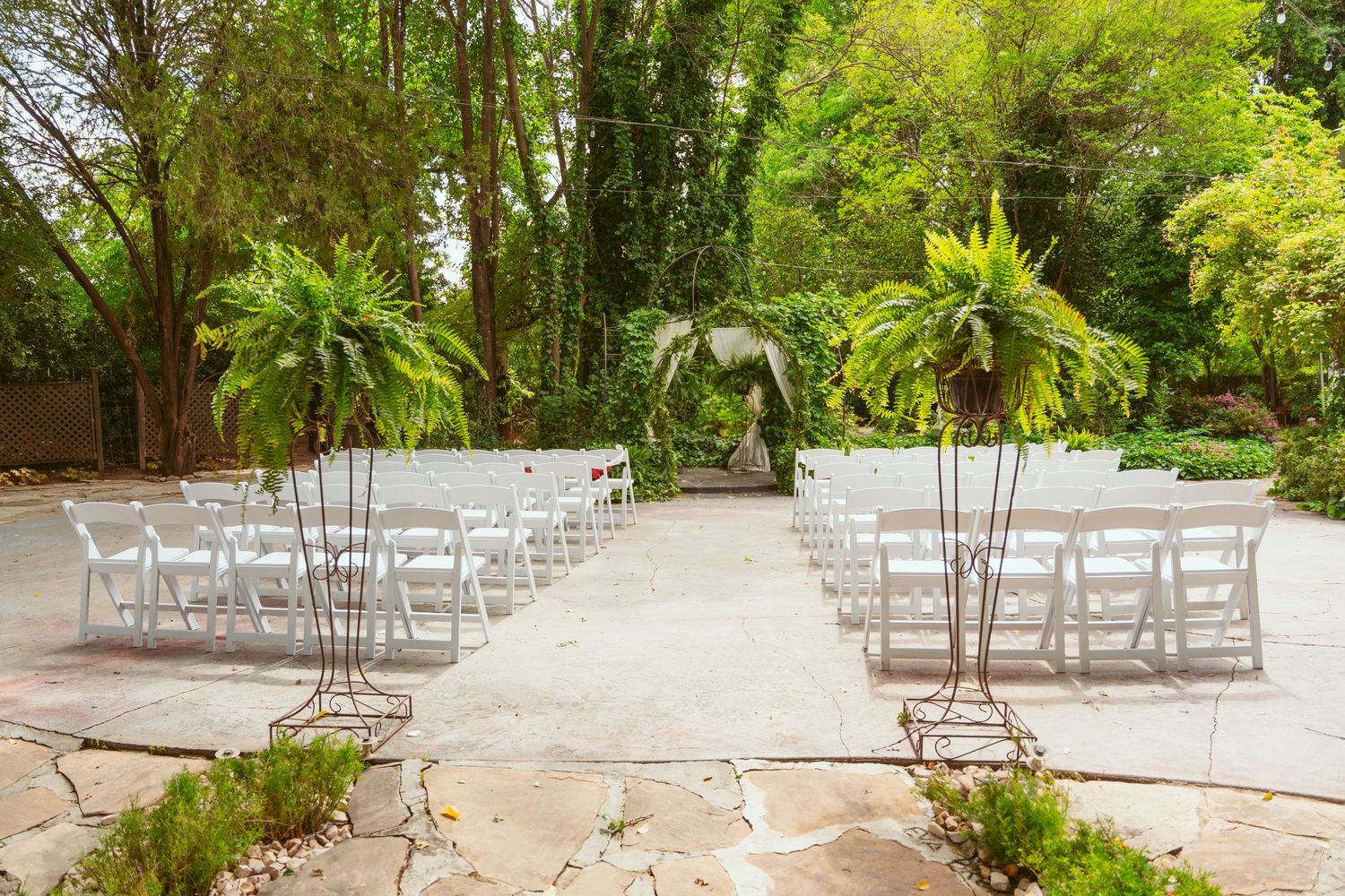 White chairs arranged in rows for an outdoor garden wedding ceremony with lush greenery and trees.