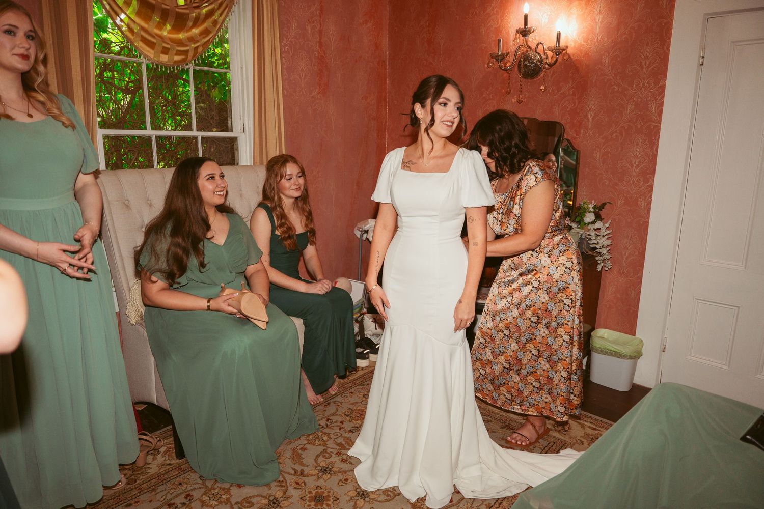 Wedding party gathered in a room with red walls and natural lighting.