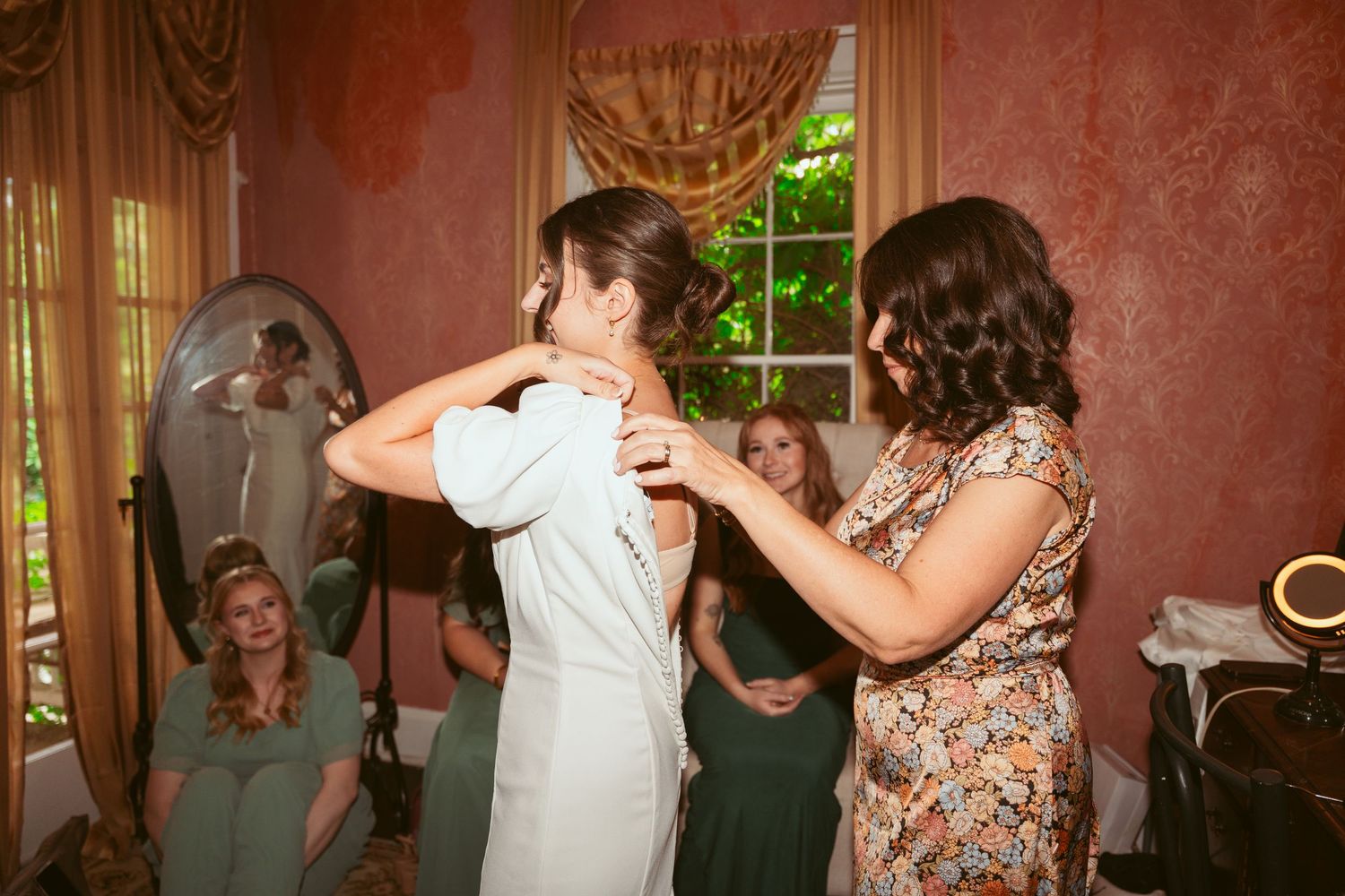 Wedding preparation moment showing dress adjustments in a vintage-style room with pink walls.