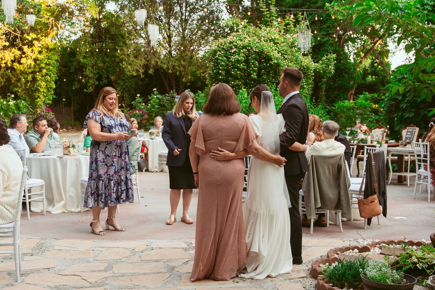 Guests mingling at an outdoor garden wedding reception with white chairs and natural decor.