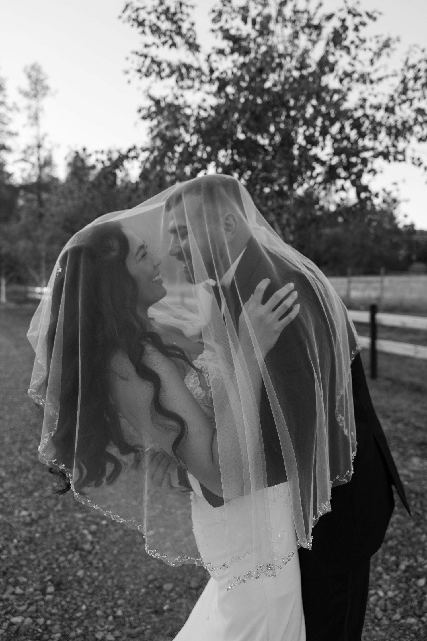 Black and white romantic portrait under flowing veil in outdoor setting.