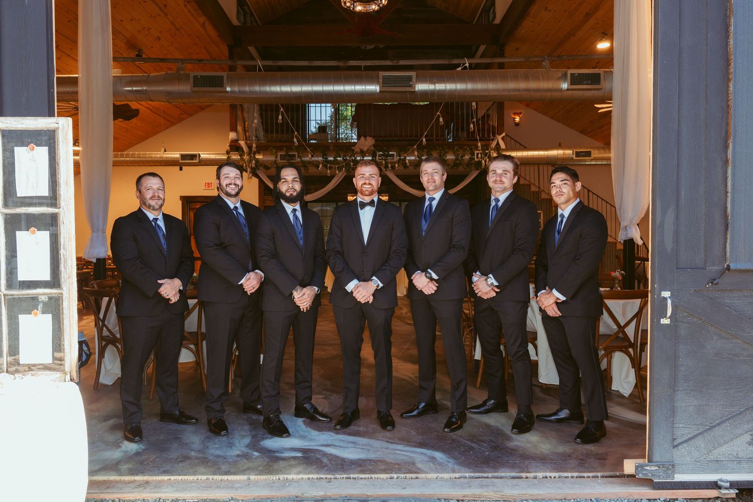 A group of groomsmen in dark suits standing together at a wedding venue entrance.