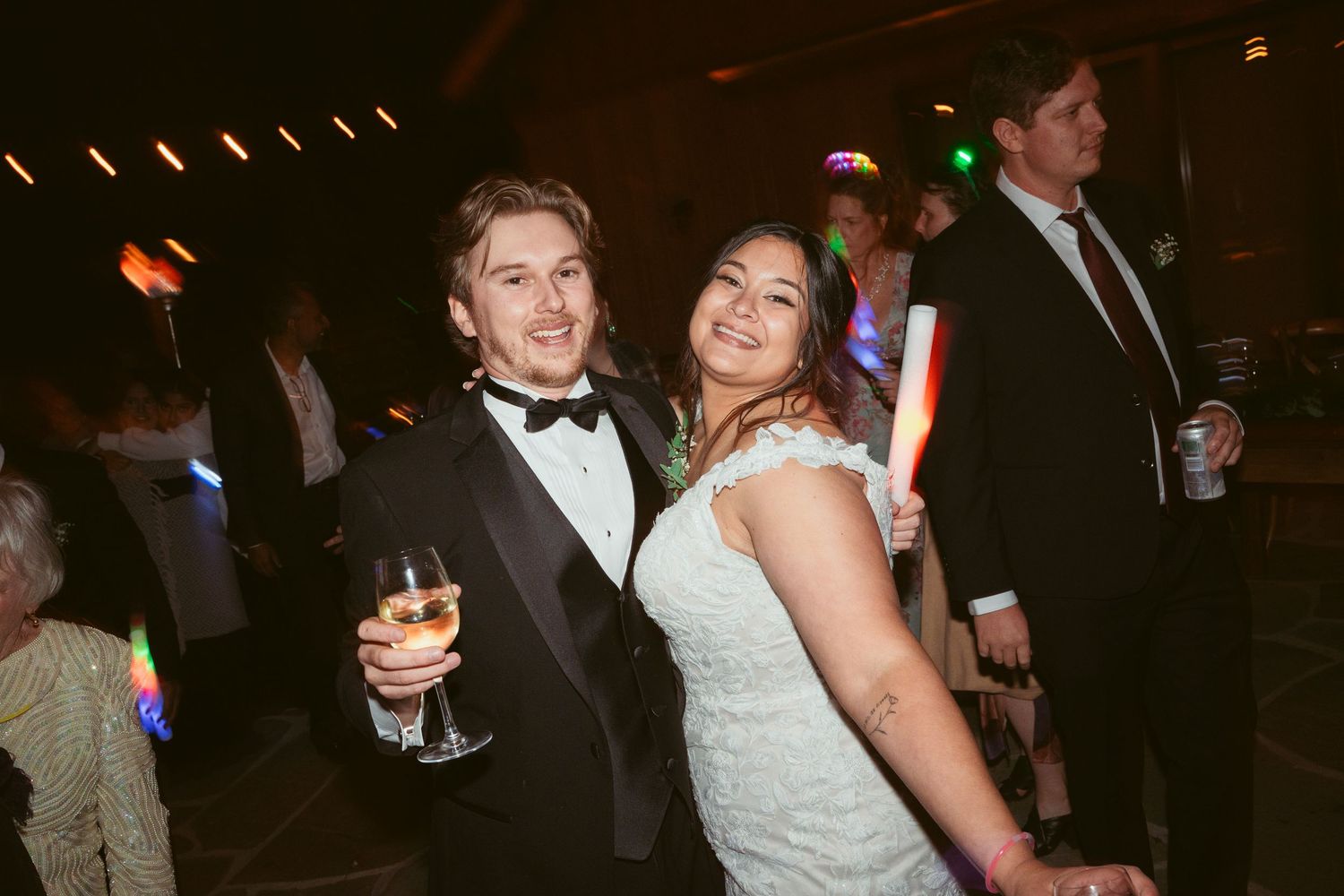 Wedding reception guests dancing and celebrating under string lights at night.