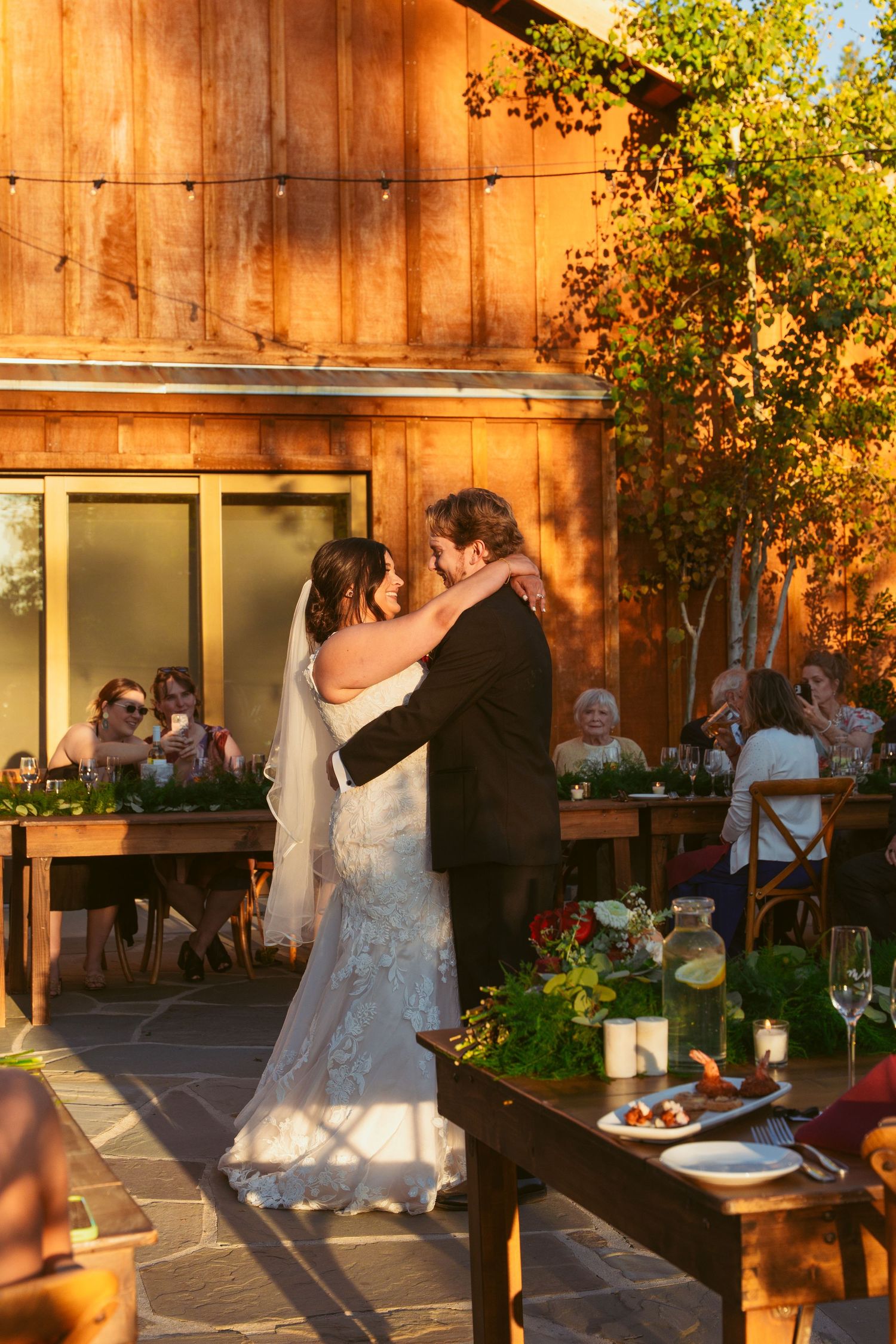 A couple dances at sunset in front of a rustic wooden barn during their wedding reception.