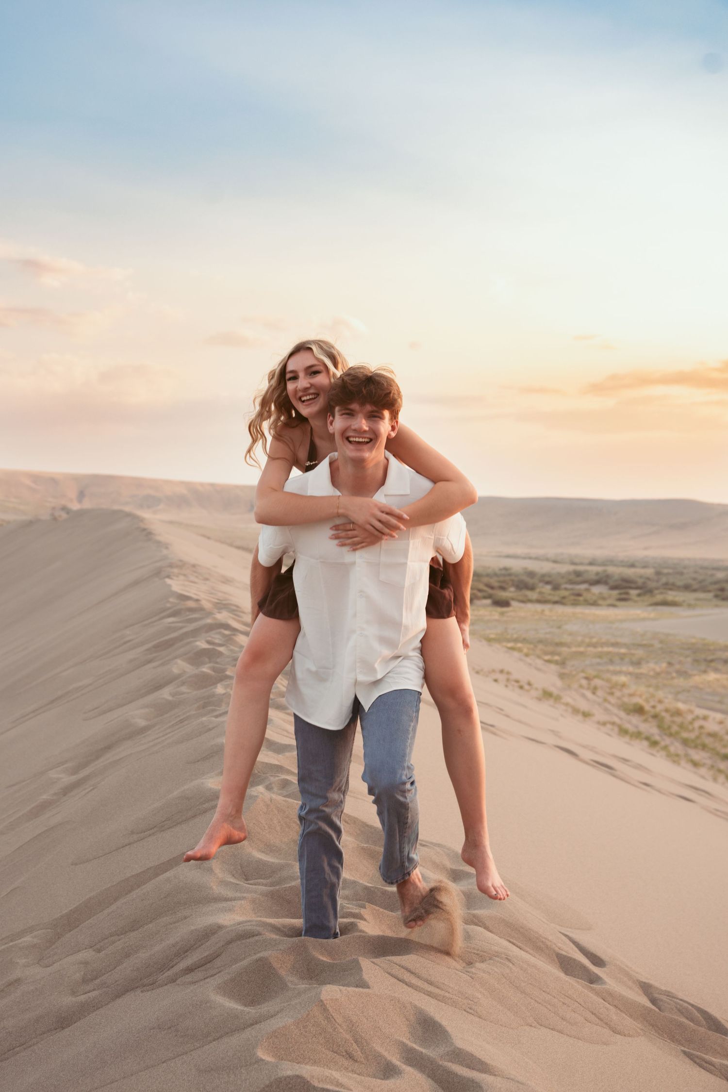 Playful couple having fun on sand dunes during sunset photoshoot.